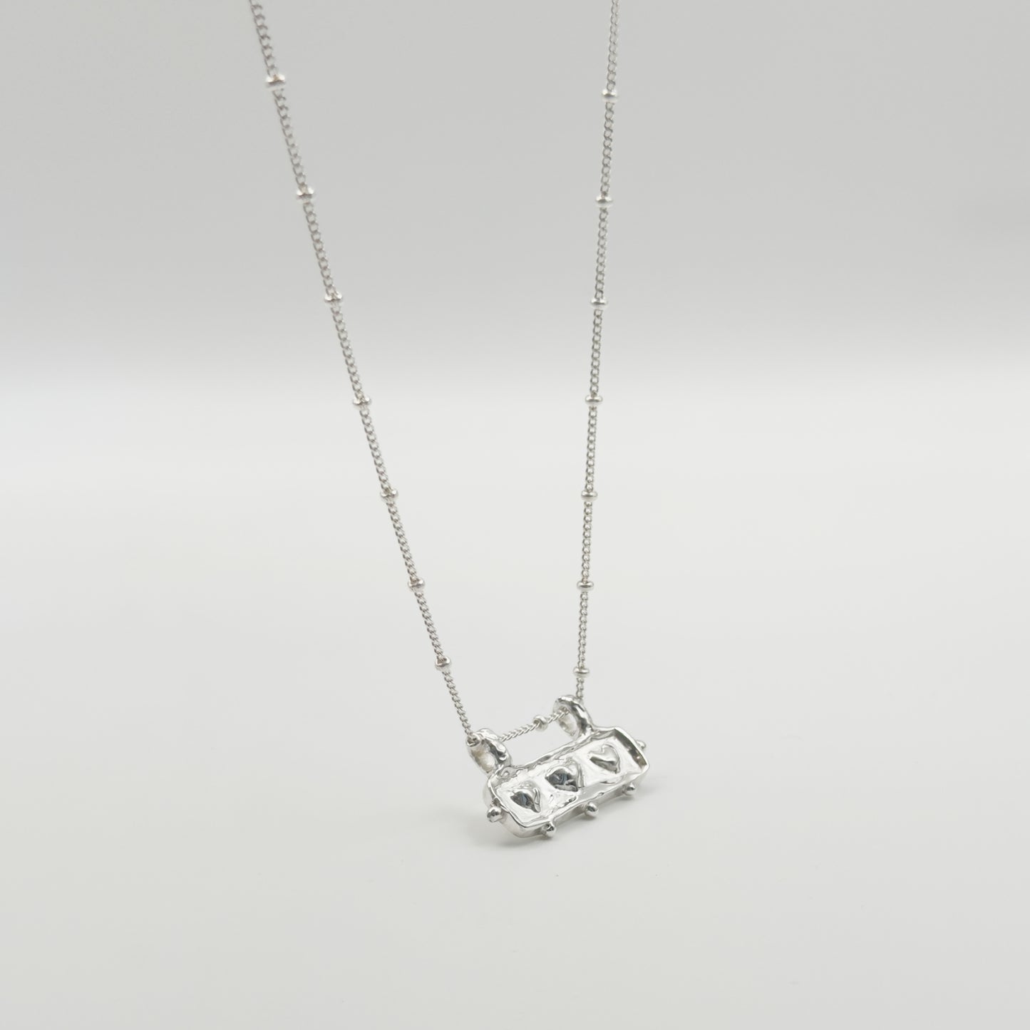 Angled front view of the Self-Love textured silver pendant on a satellite chain, pictured on a light plain background.