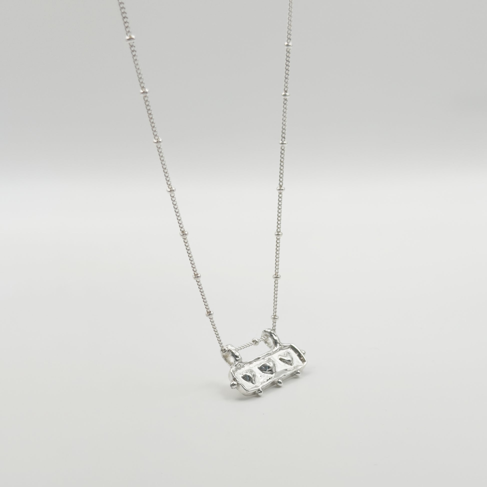 Angled front view of the Self-Love textured silver pendant on a satellite chain, pictured on a light plain background.