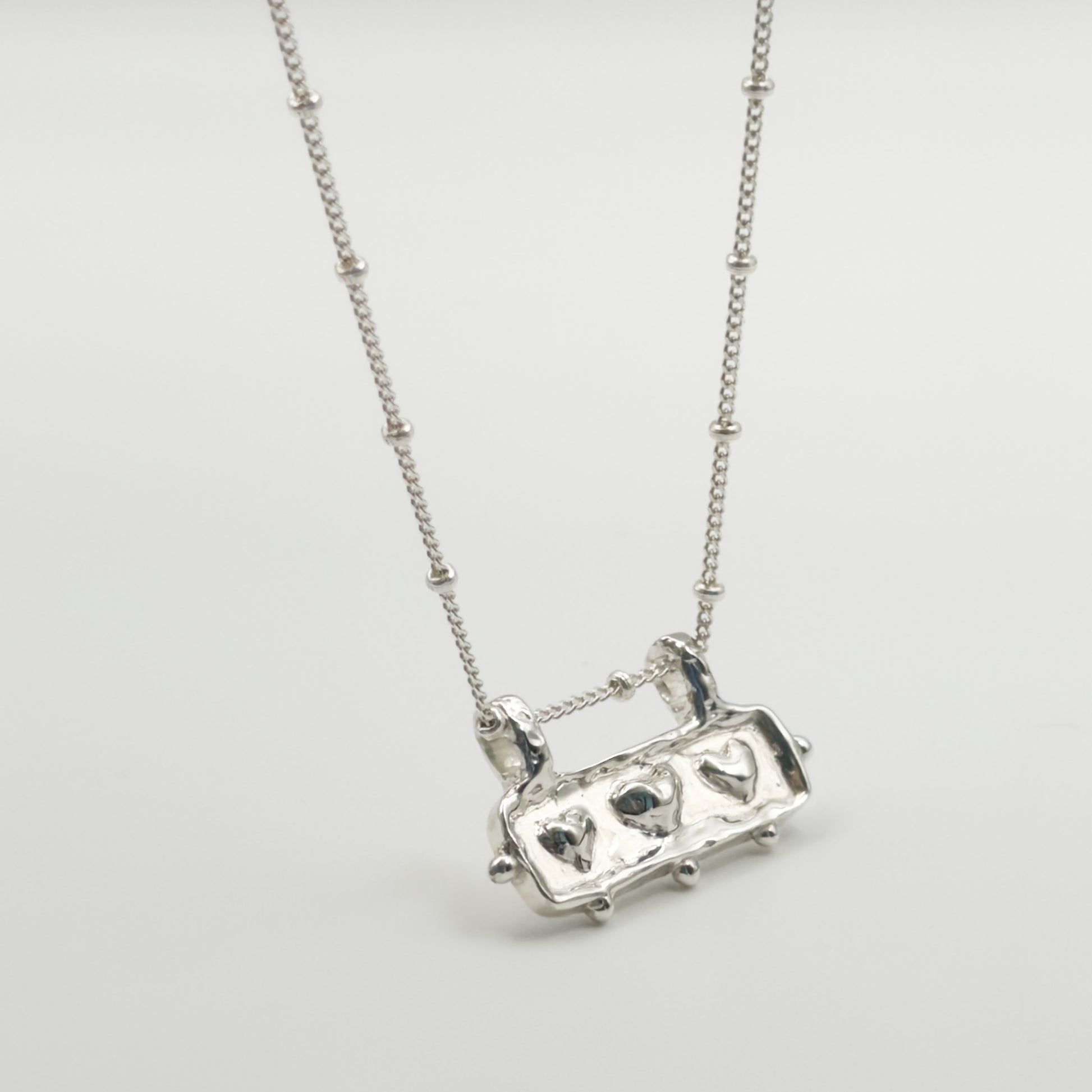Close-up view of the Self-Love textured silver pendant on a satellite chain, pictured on a light plain background.