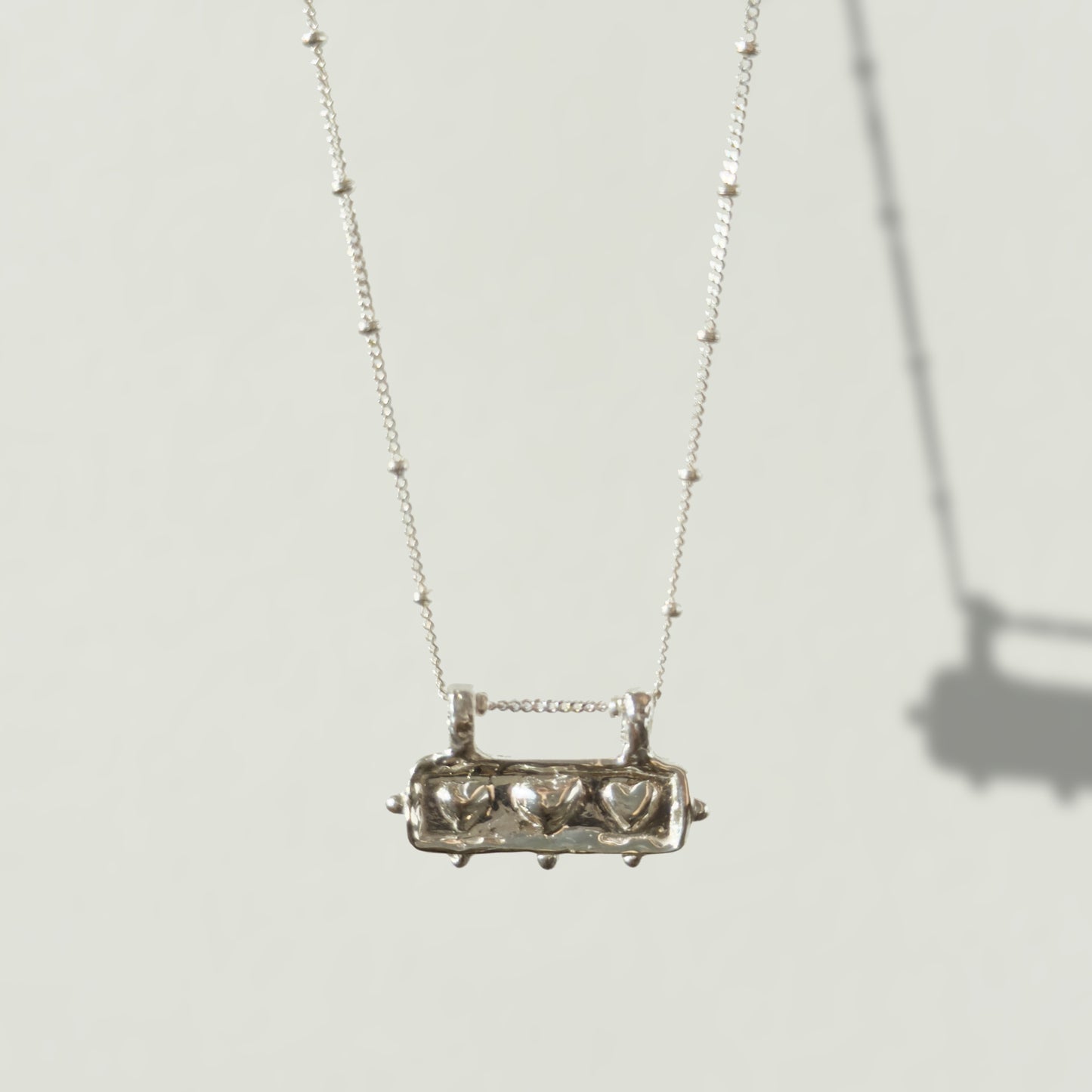 Front view of the Self-Love textured silver pendant on a satellite chain, pictured on a light plain background.