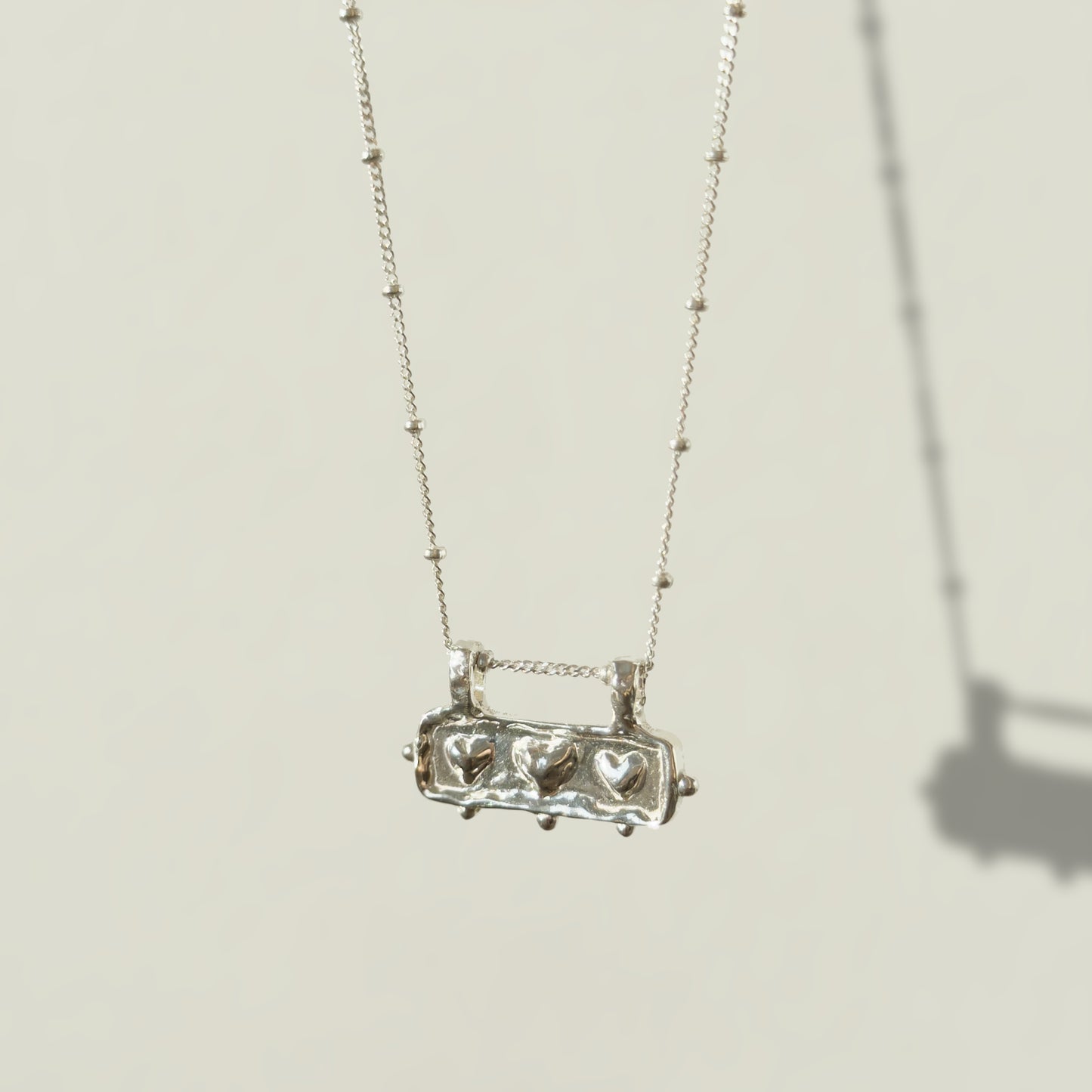 Angled front view of the Self-Love textured silver pendant on a satellite chain, pictured on a light plain background.