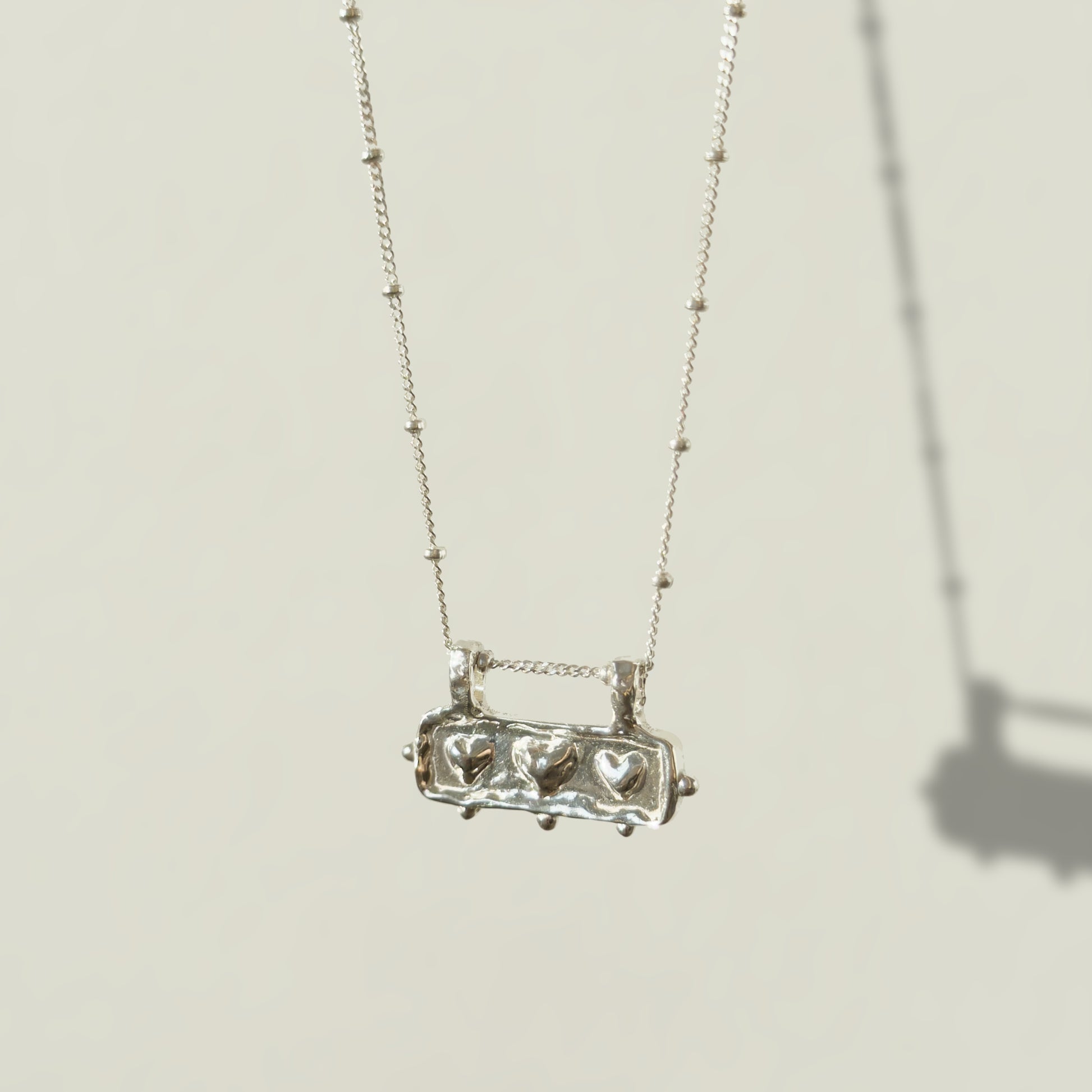 Angled front view of the Self-Love textured silver pendant on a satellite chain, pictured on a light plain background.