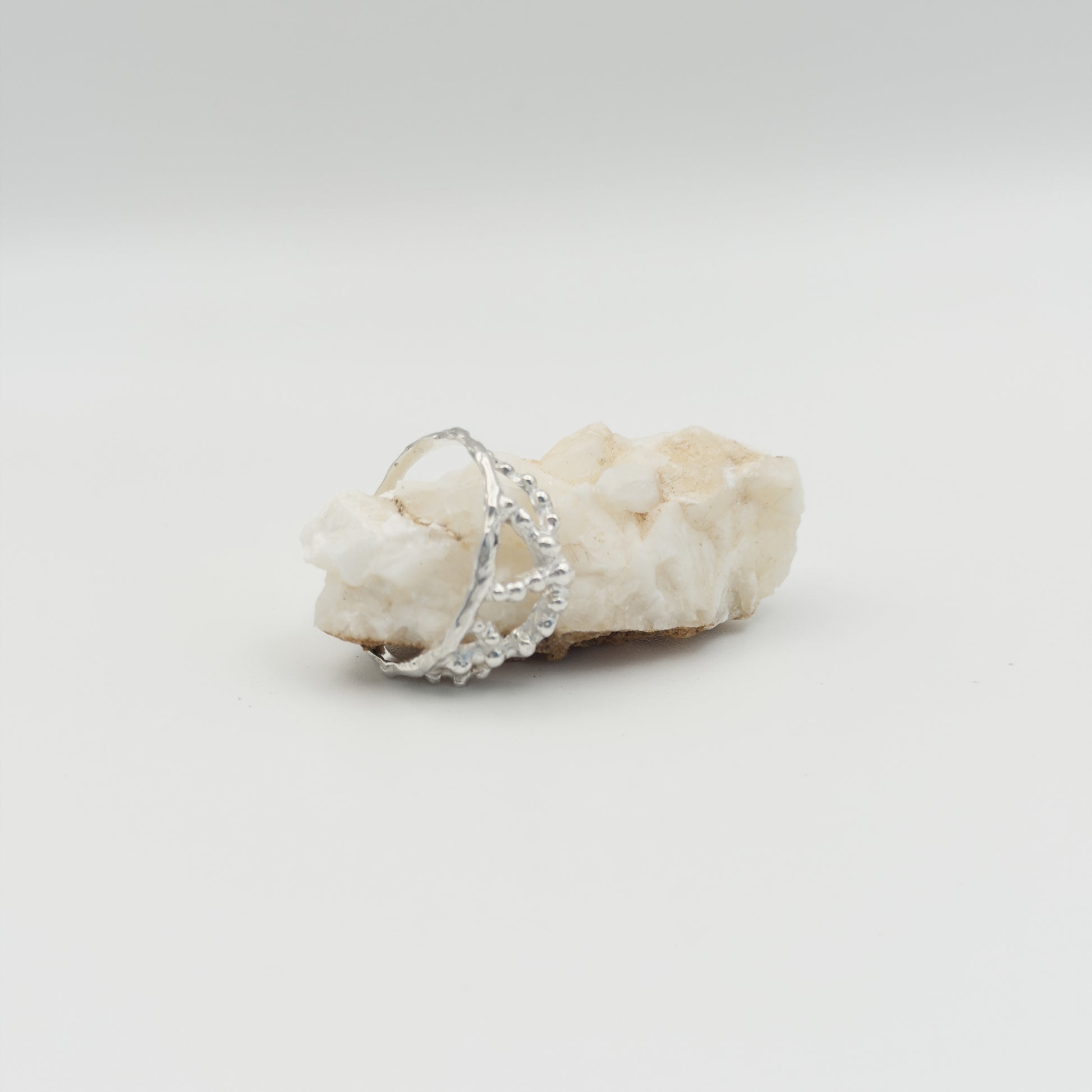 Angled front view of the Sequence textured silver ring, pictured on a light plain background next to a piece of beige rock.