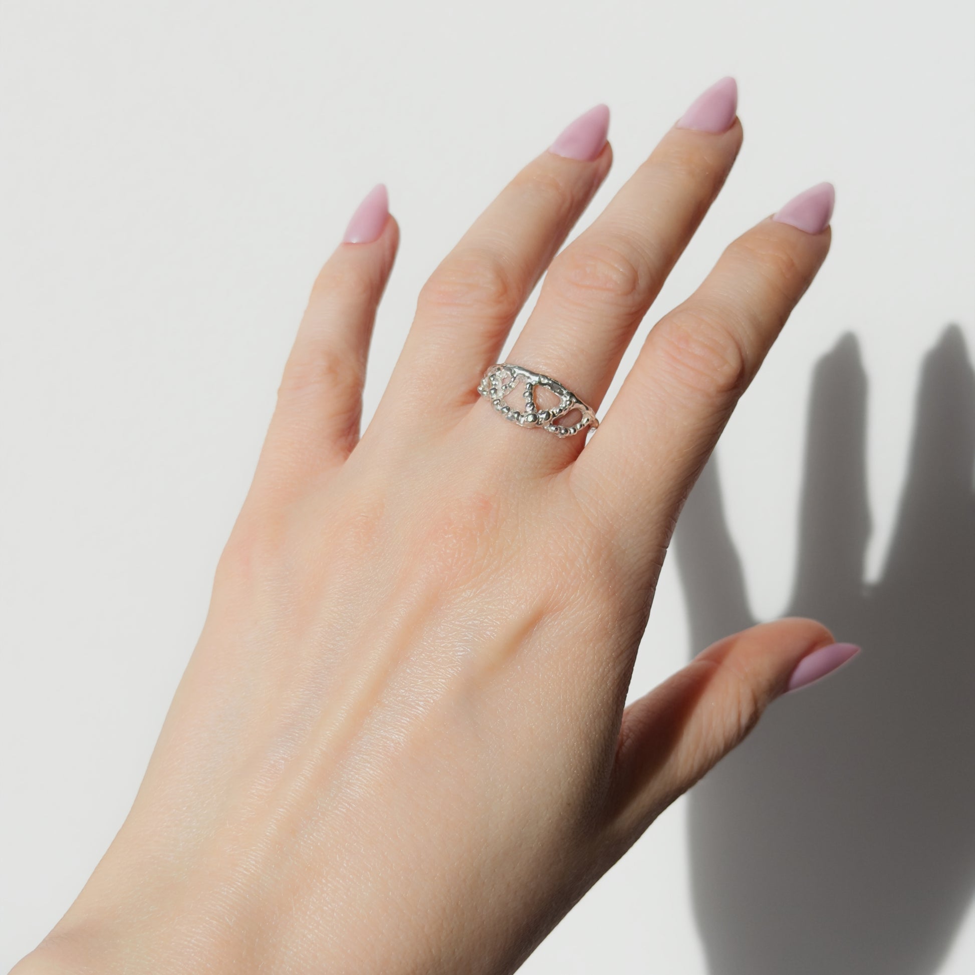 Hand wearing the Sequence textured silver ring on a plain background.