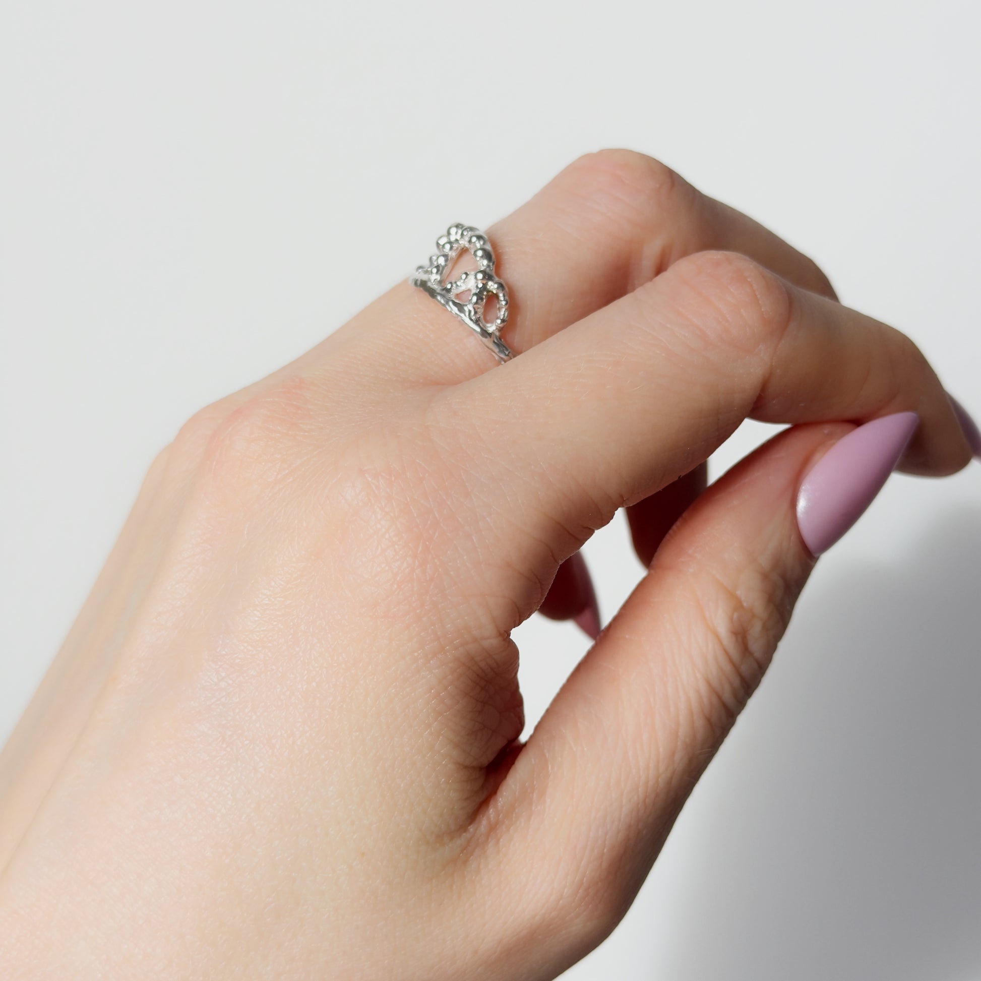 Hand wearing the Sequence textured silver ring on a plain background.