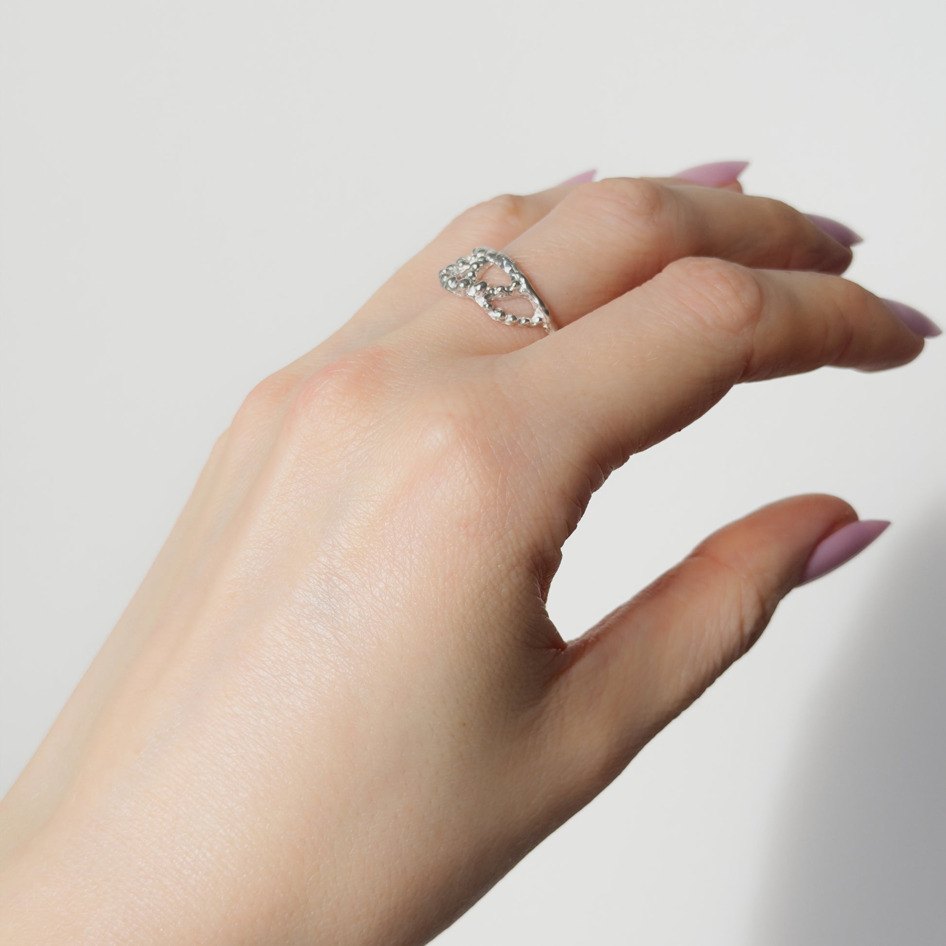 Hand wearing the Sequence textured silver ring on a plain background.