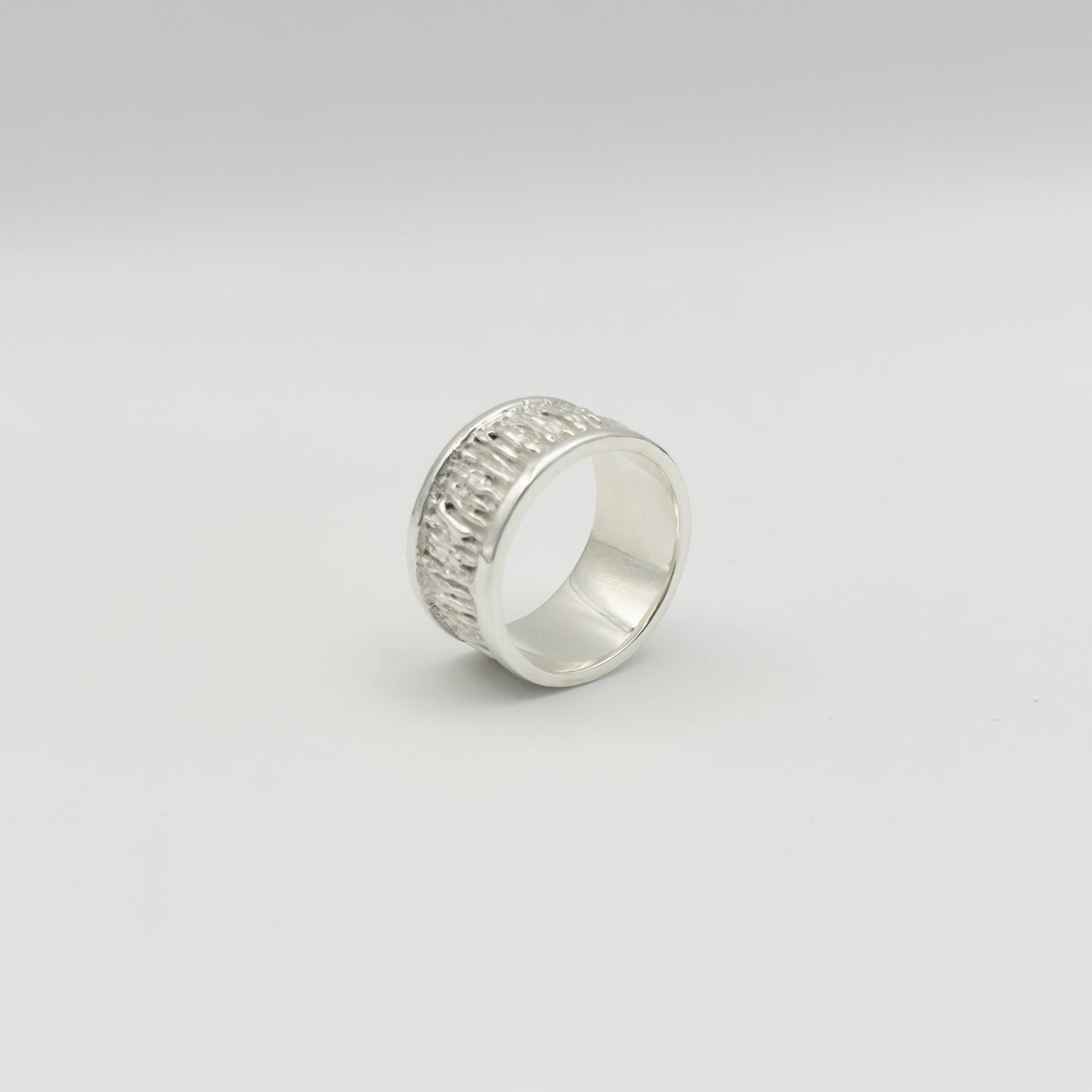 Angled side view of the Solace textured silver ring, pictured on a light plain background.