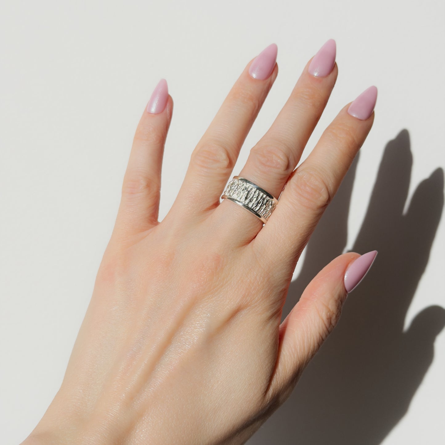 Hand wearing the Solace textured silver ring on a plain background.