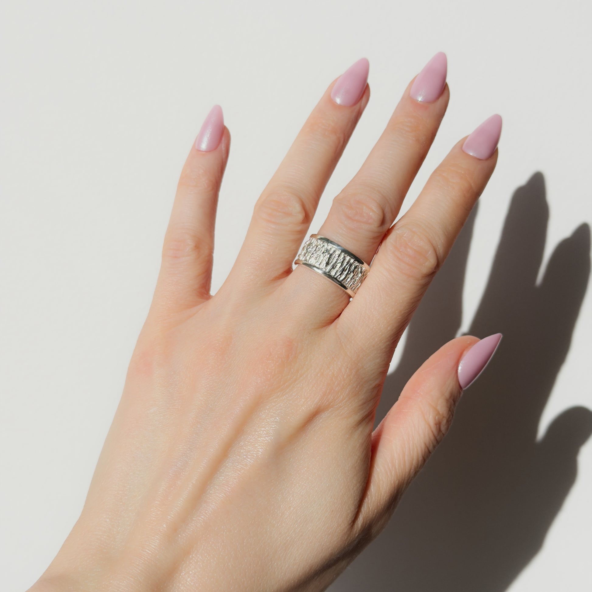 Hand wearing the Solace textured silver ring on a plain background.