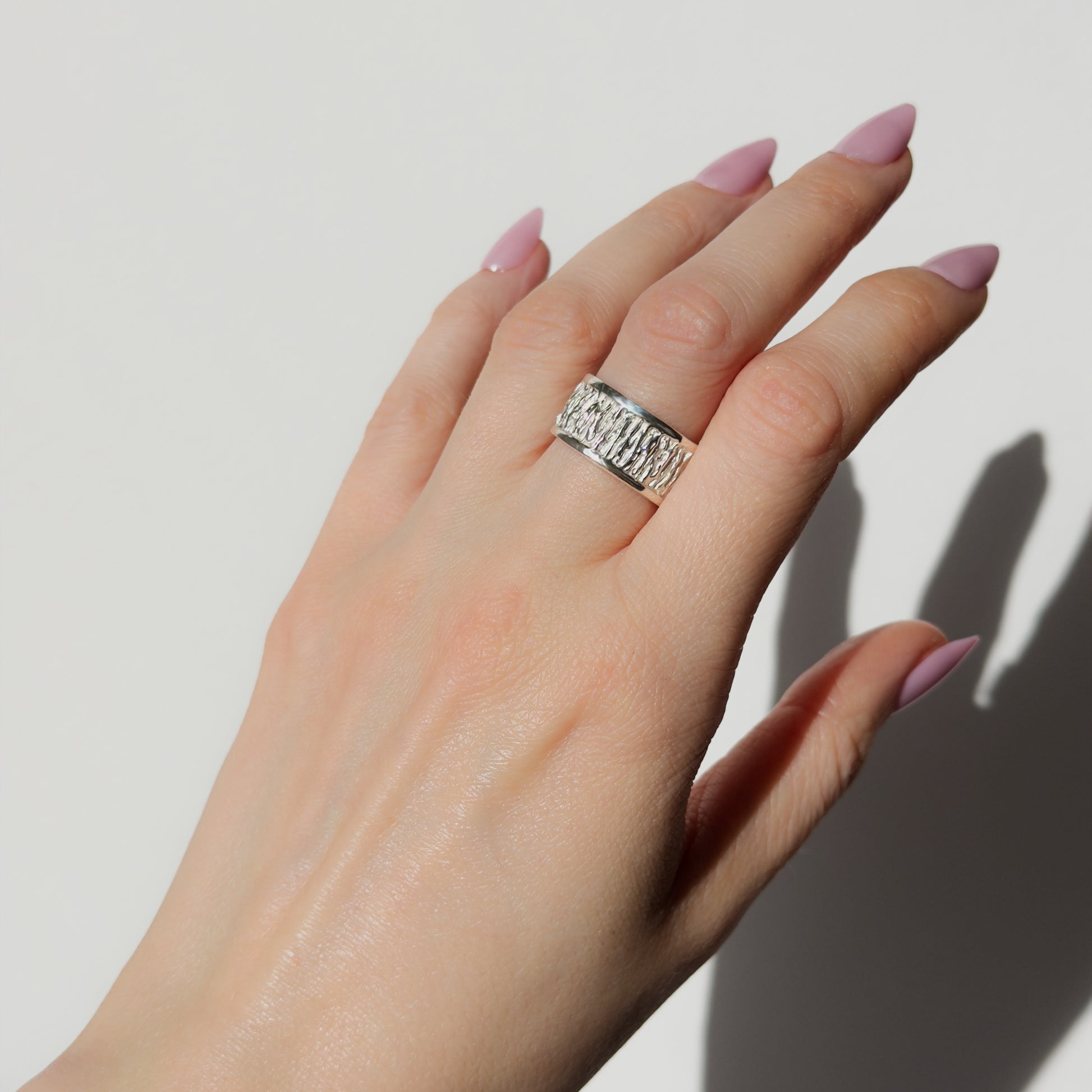 Hand wearing the Solace textured silver ring on a plain background.