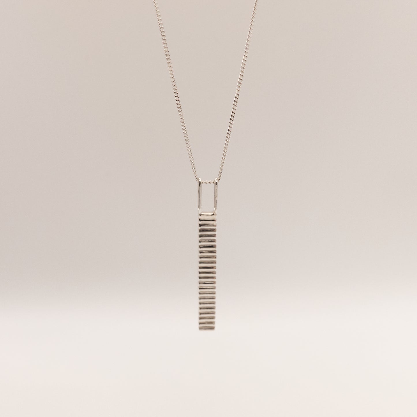 Front view of the Thread textured silver pendant on a curb chain, pictured on a light plain background.