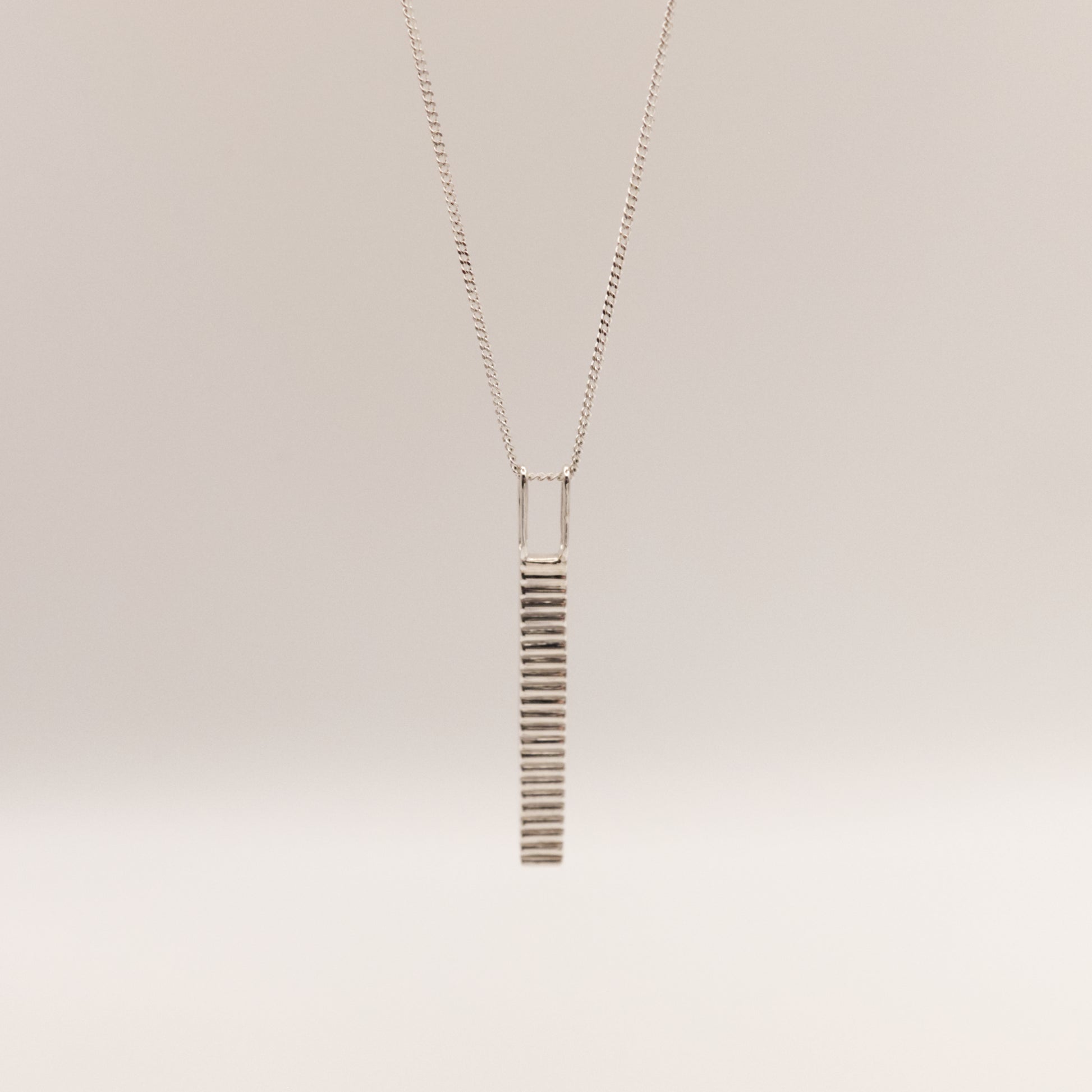 Front view of the Thread textured silver pendant on a curb chain, pictured on a light plain background.