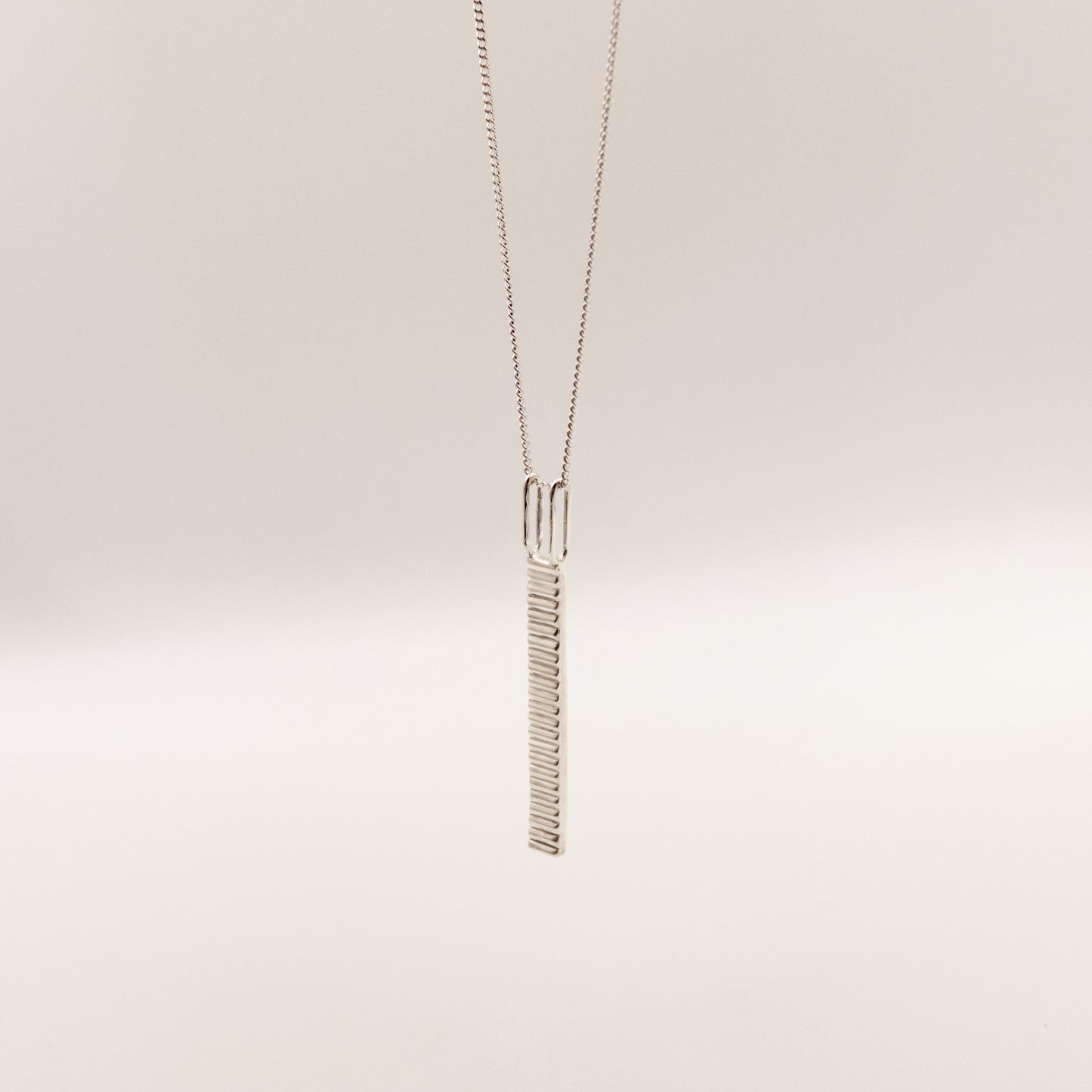 Angled front view of the Thread textured silver pendant on a curb chain, pictured on a light plain background.