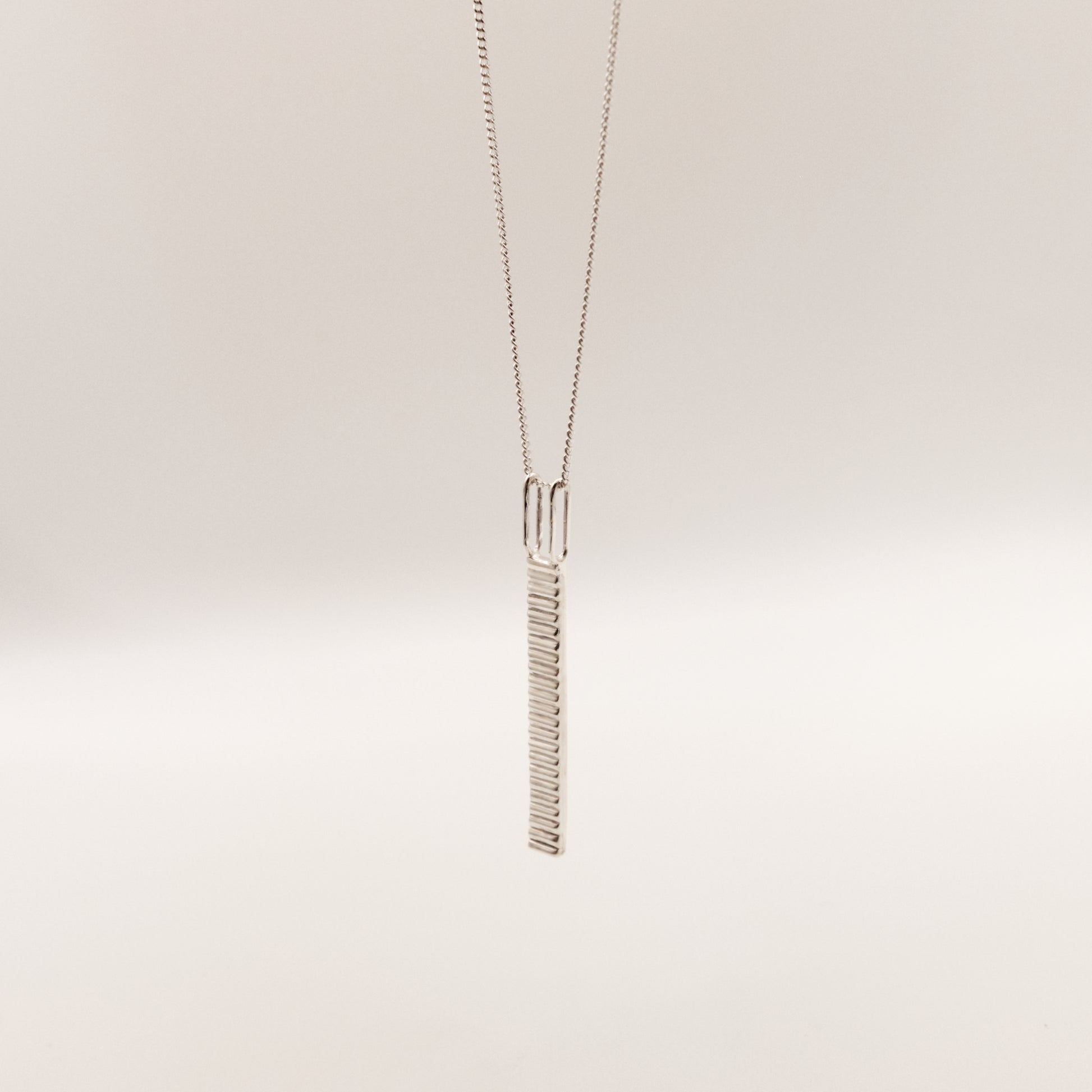 Angled front view of the Thread textured silver pendant on a curb chain, pictured on a light plain background.