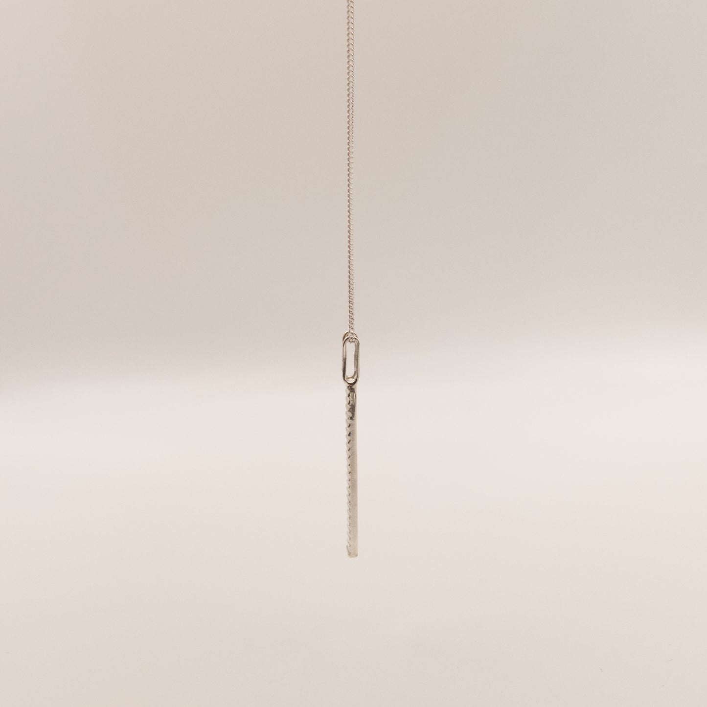 Side view of the Thread textured silver pendant on a curb chain, pictured on a light plain background.