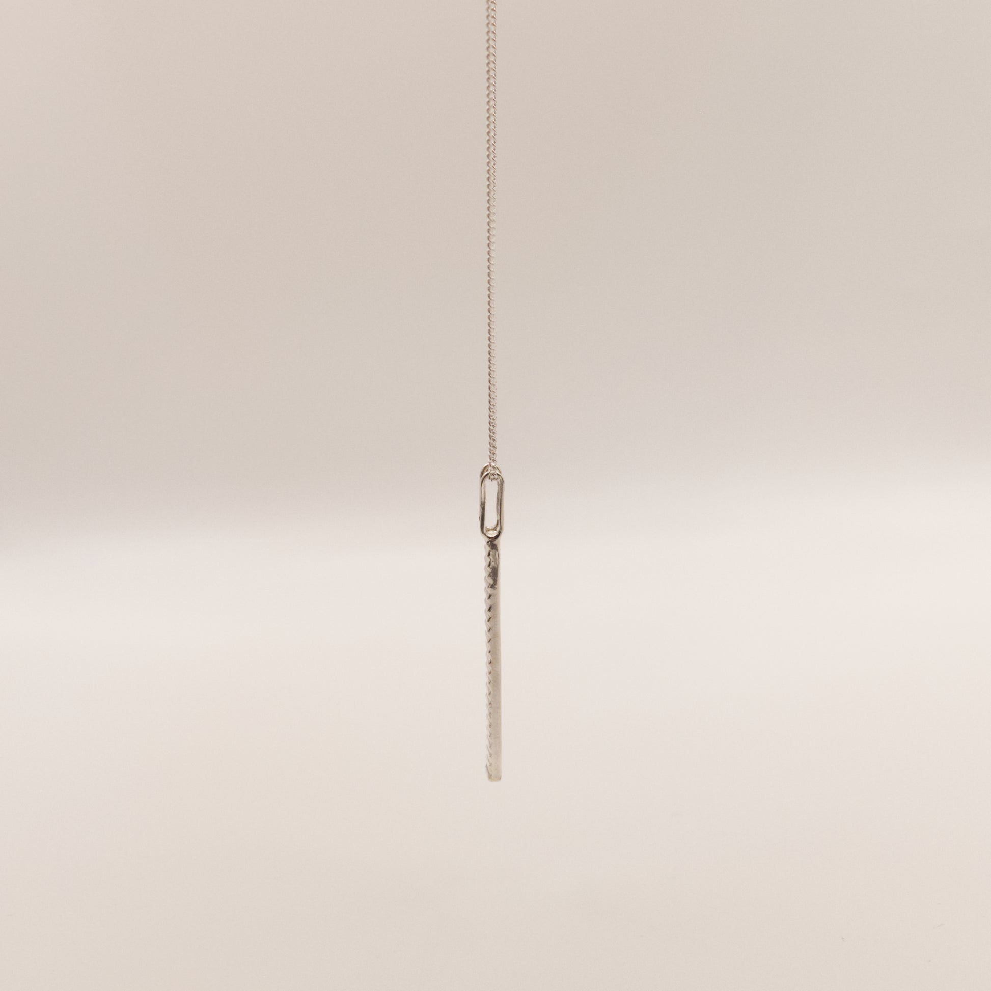 Side view of the Thread textured silver pendant on a curb chain, pictured on a light plain background.