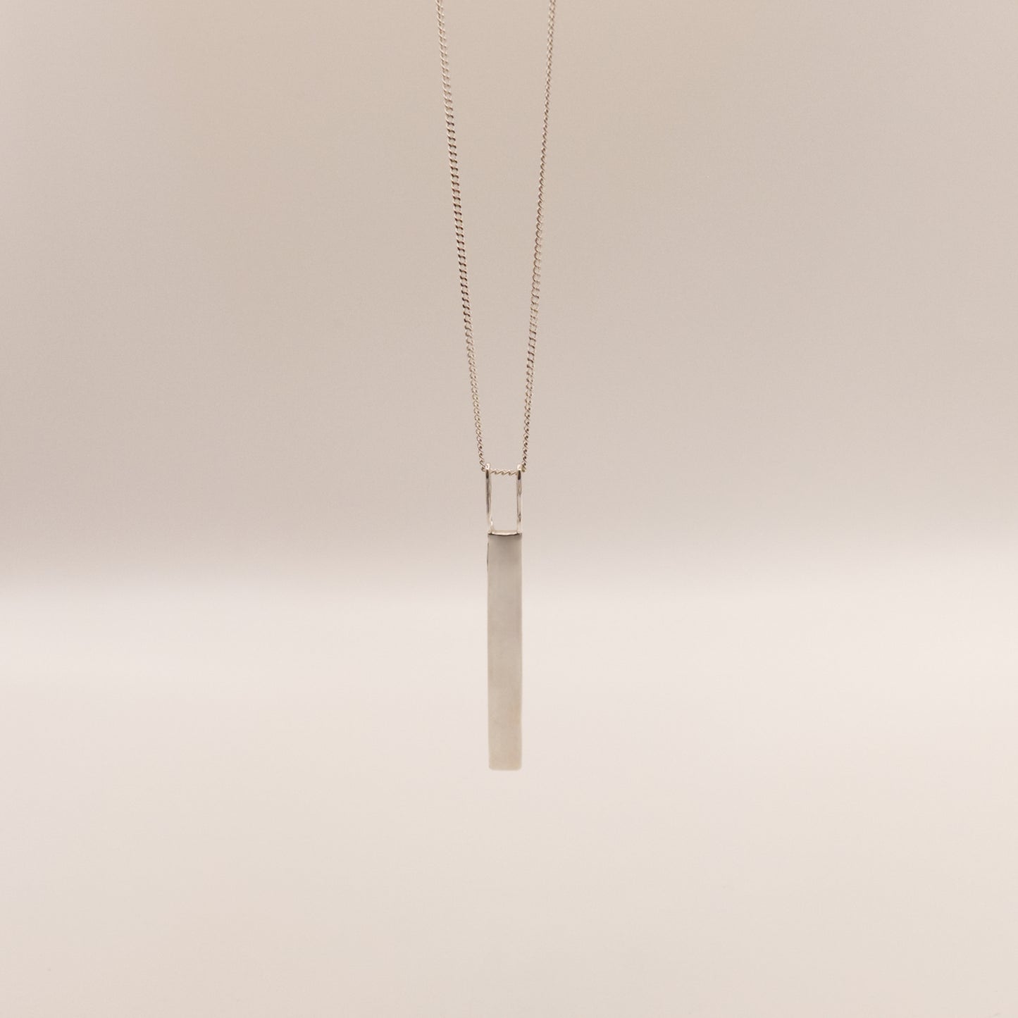Back view of the Thread textured silver pendant on a curb chain, pictured on a light plain background.