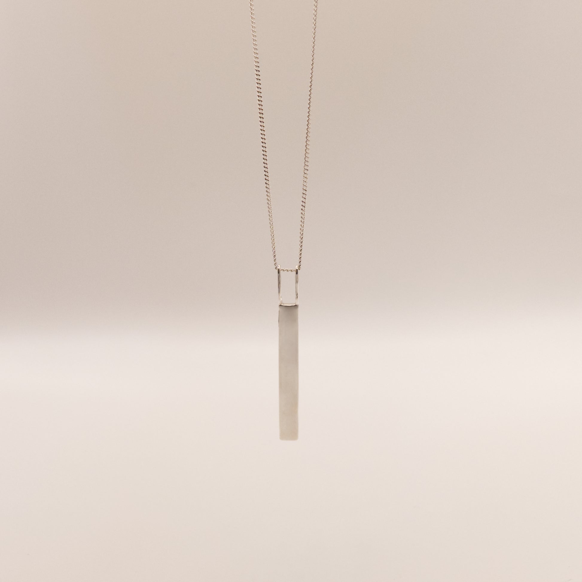 Back view of the Thread textured silver pendant on a curb chain, pictured on a light plain background.