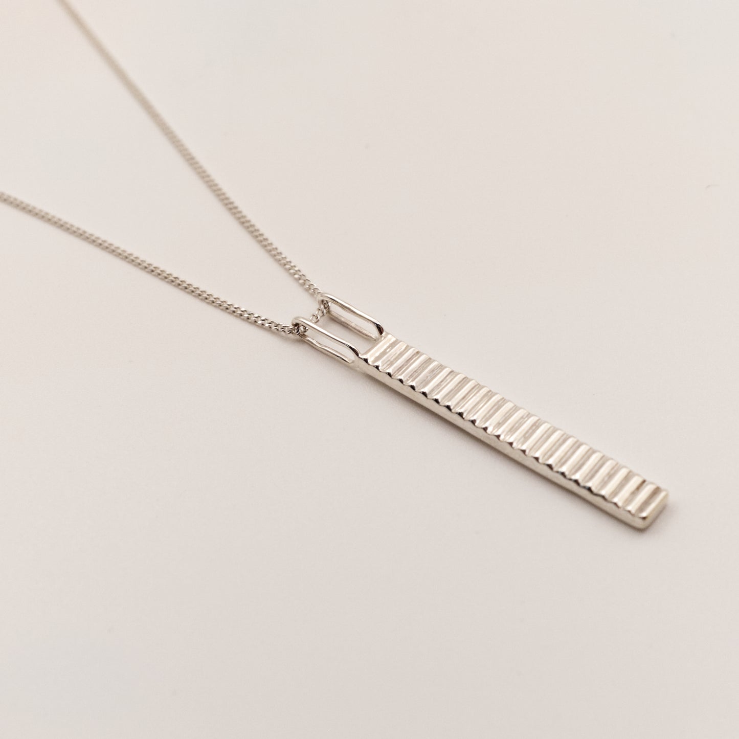 Close-up view of the Thread textured silver pendant on a curb chain, pictured on a light plain background.