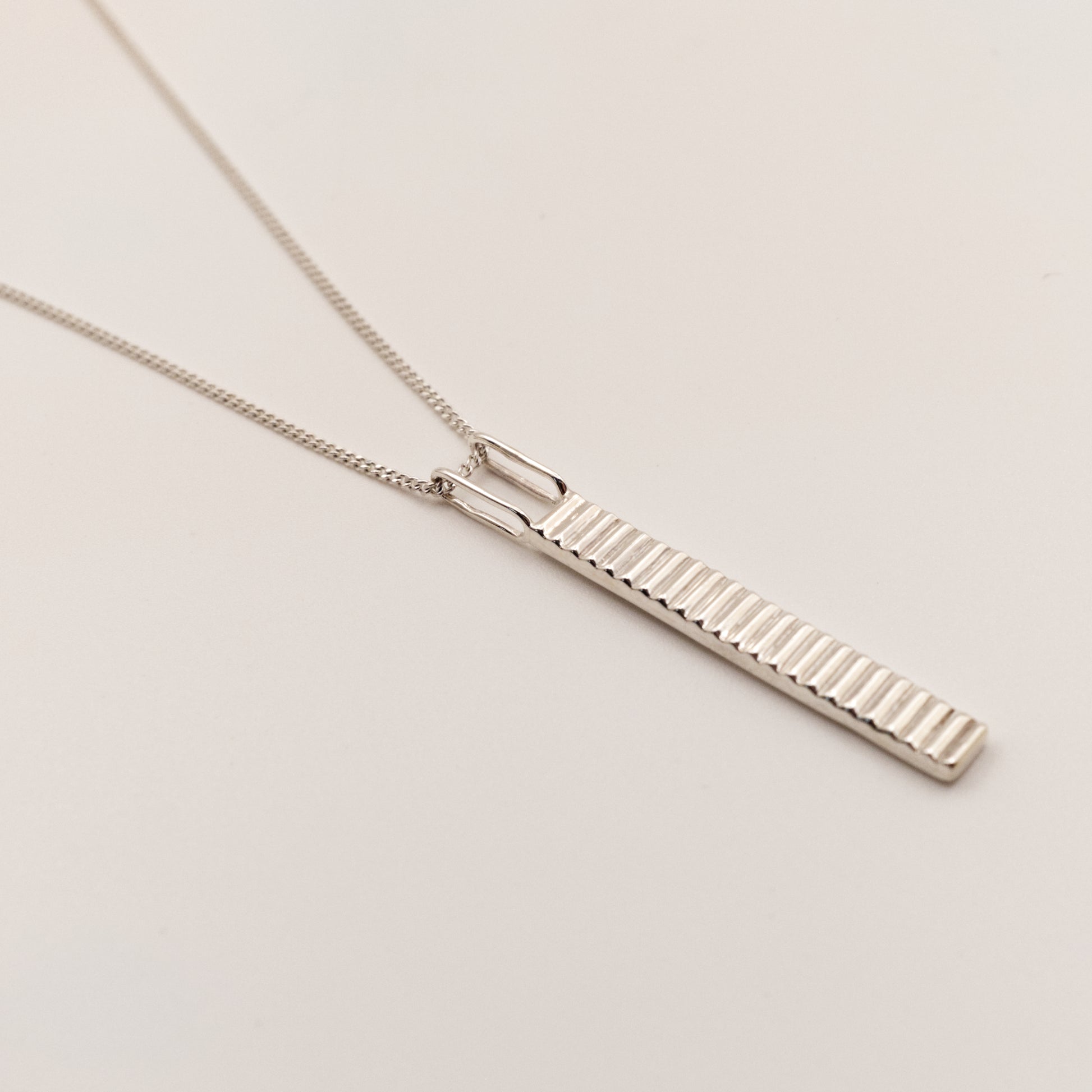Close-up view of the Thread textured silver pendant on a curb chain, pictured on a light plain background.