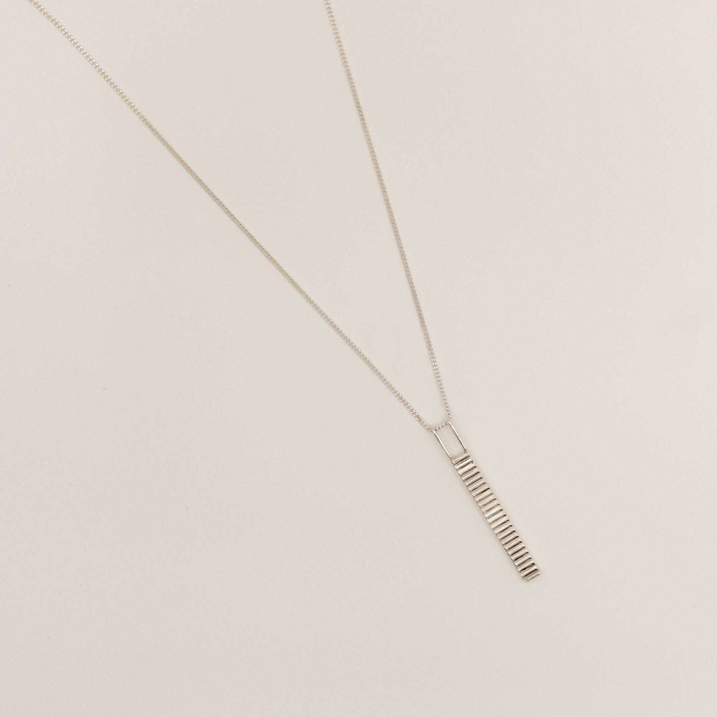 Top view of the Thread textured silver pendant on a curb chain, pictured on a light plain background.