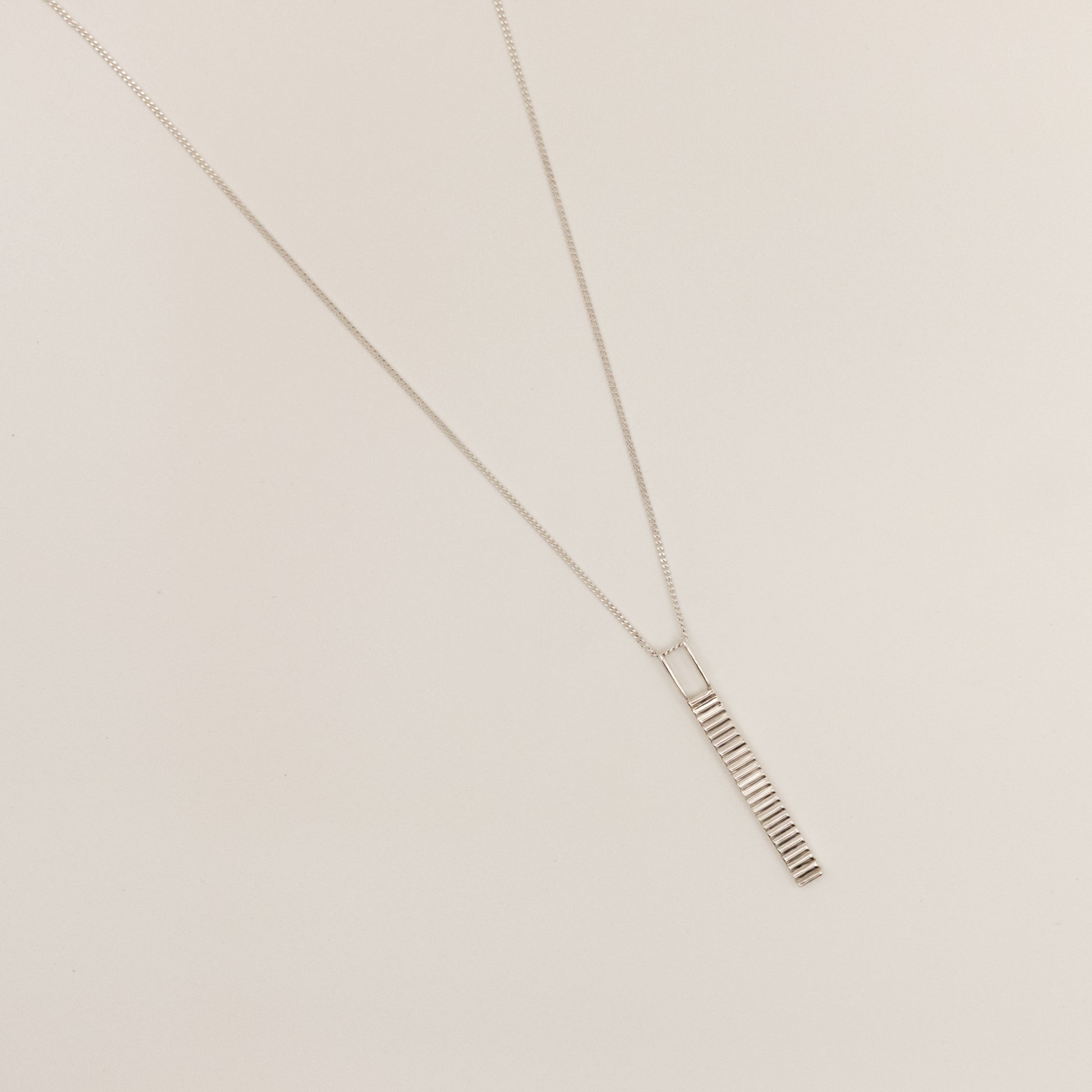 Top view of the Thread textured silver pendant on a curb chain, pictured on a light plain background.