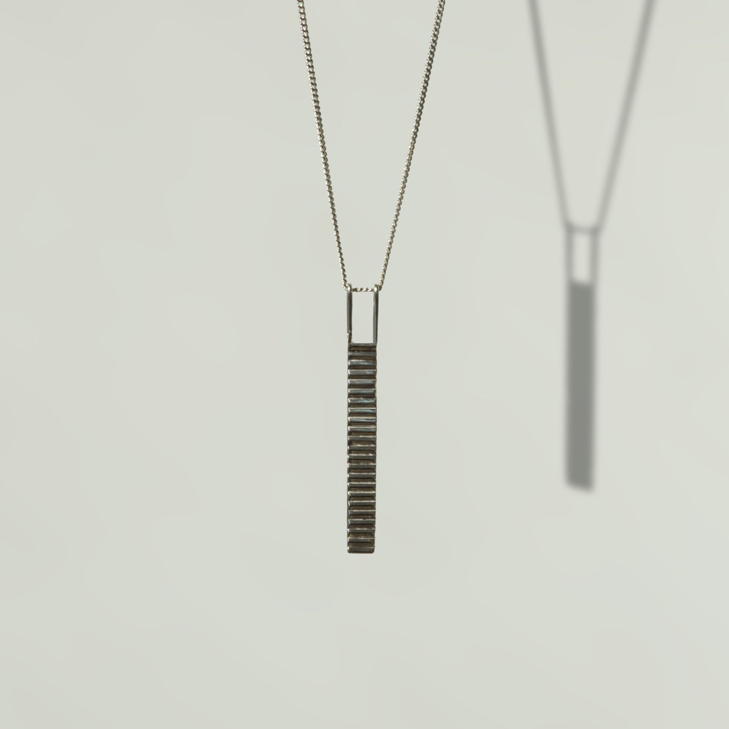 Front view of the Thread textured silver pendant on a curb chain, pictured on a light plain background.