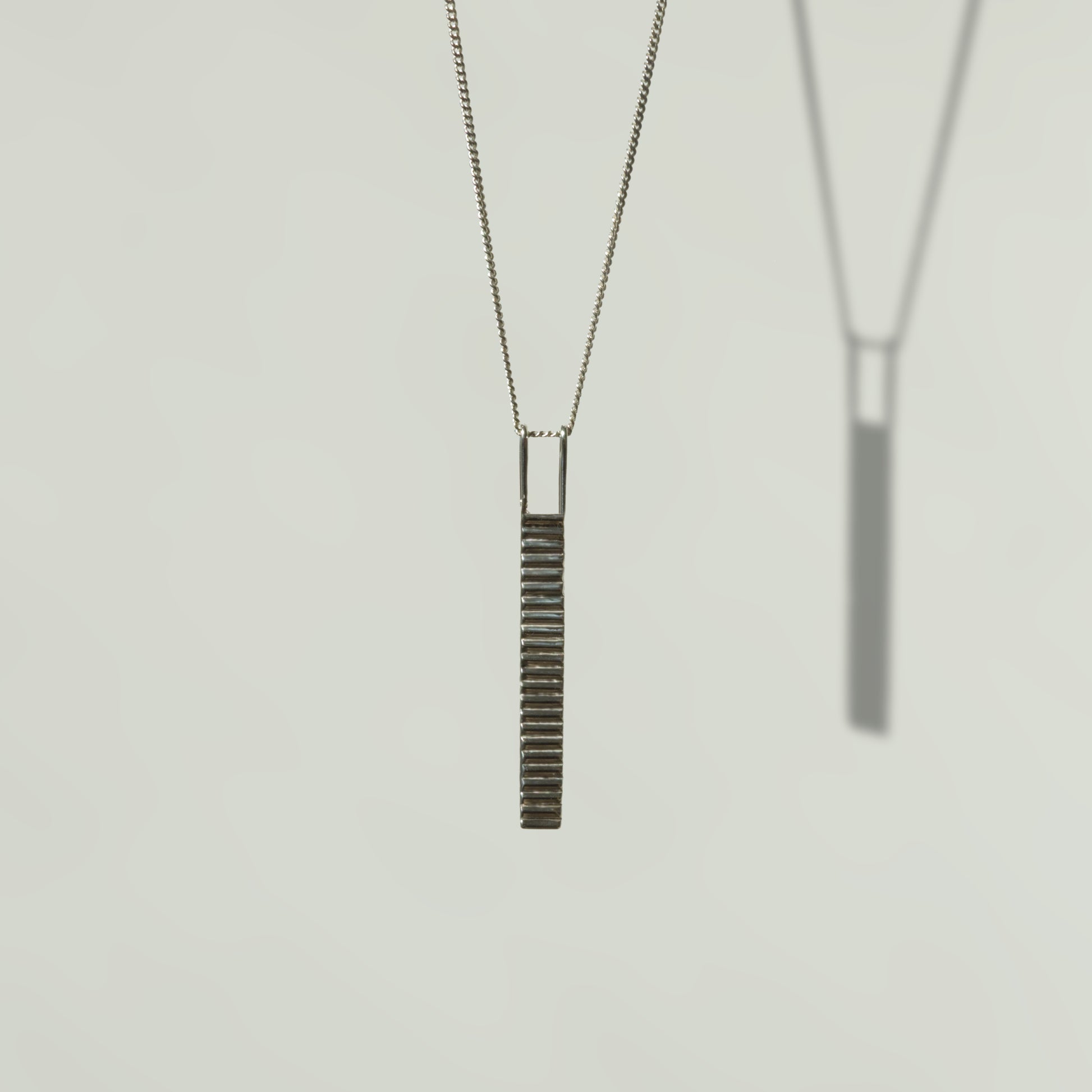 Front view of the Thread textured silver pendant on a curb chain, pictured on a light plain background.