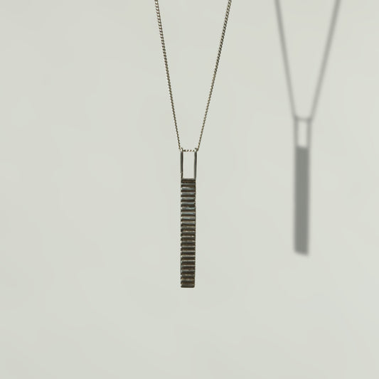 Front view of the Thread textured silver pendant on a curb chain, pictured on a light plain background.