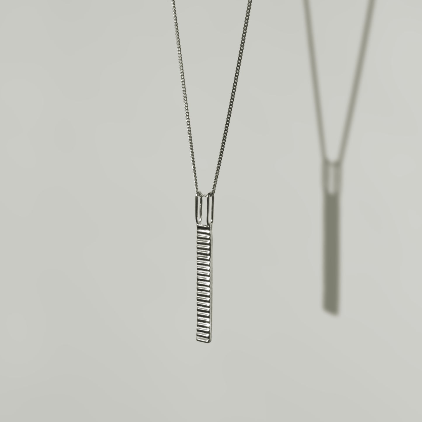 Angled front view of the Thread textured silver pendant on a curb chain, pictured on a light plain background.