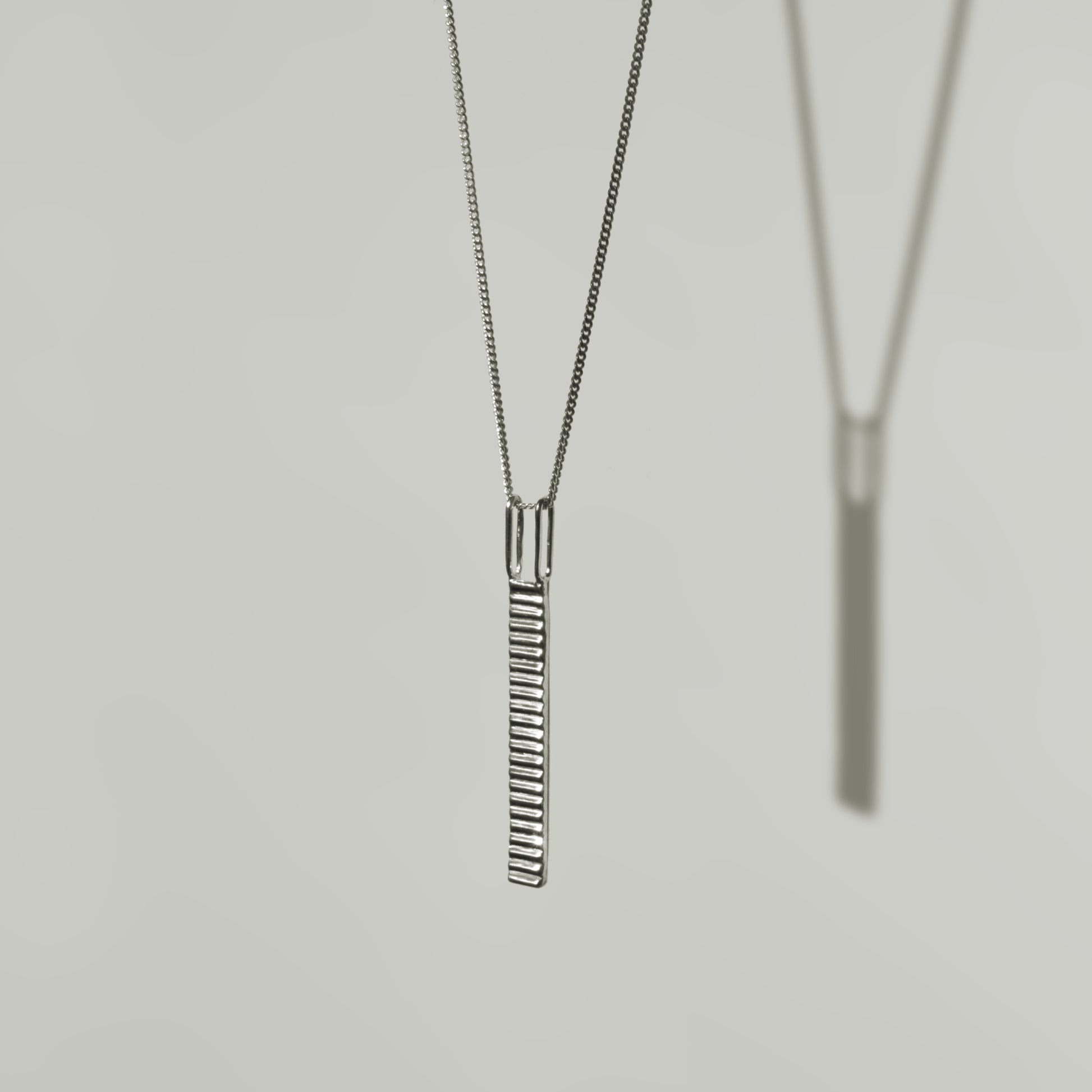 Angled front view of the Thread textured silver pendant on a curb chain, pictured on a light plain background.