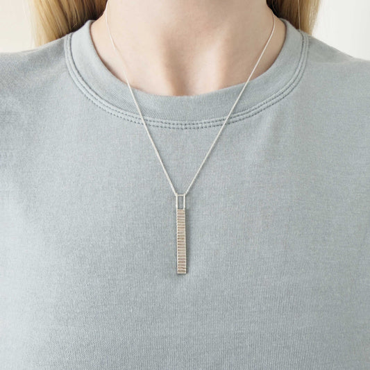 Thread textured silver pendant on a curb chain. Pictured on a person wearing a light blue-gray top.