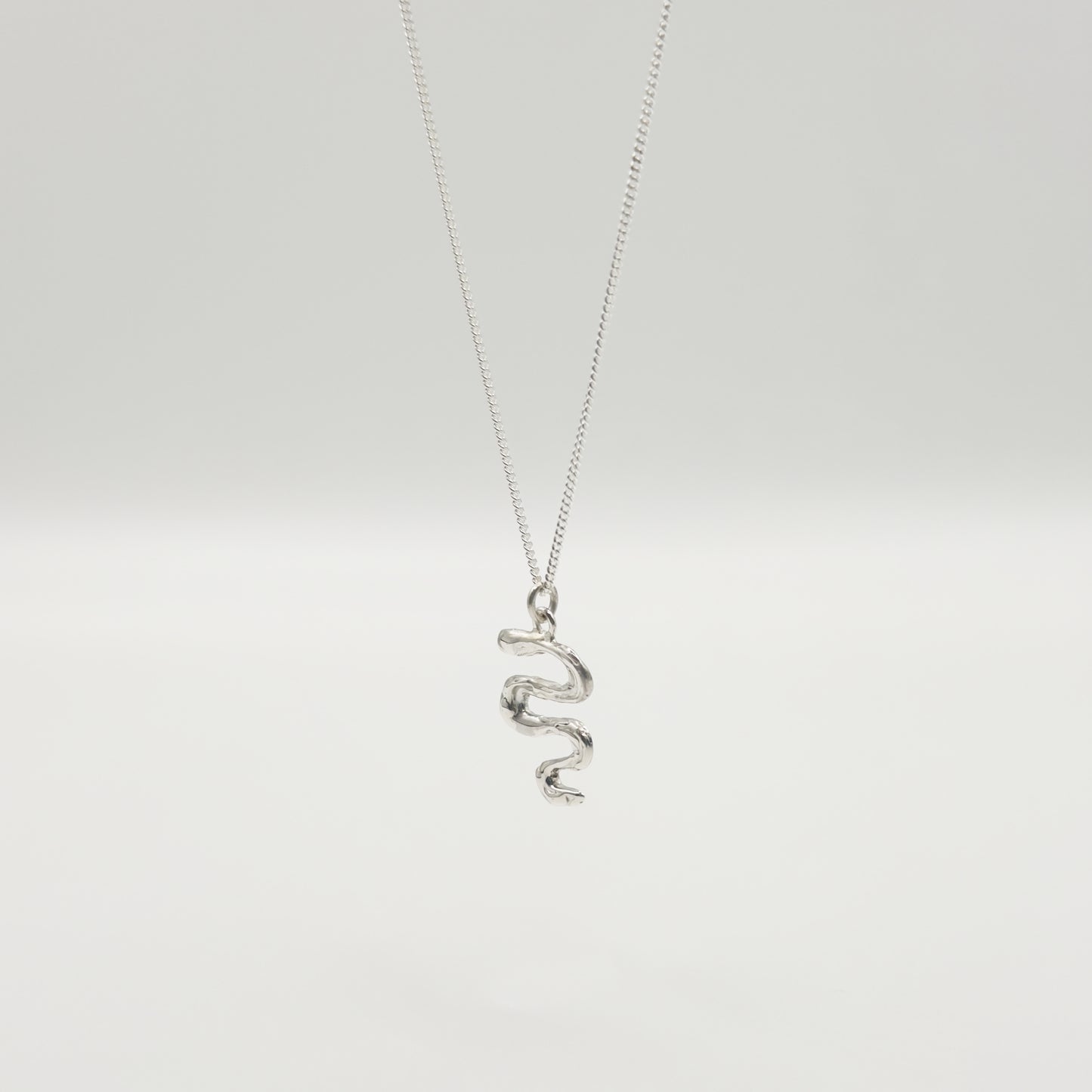 Angled front view of the Unfold textured silver necklace, pictured on a light plain background.