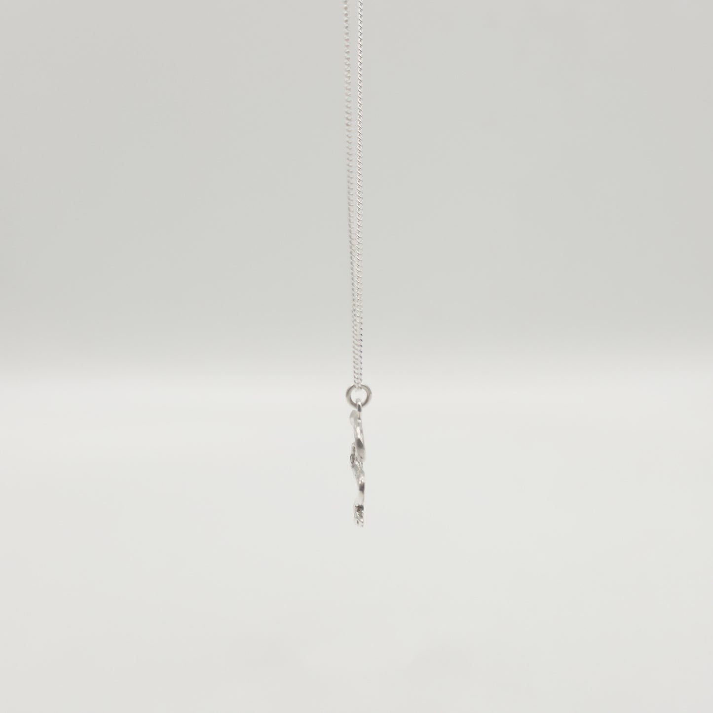 Side view of the Unfold textured silver necklace, pictured on a light plain background.