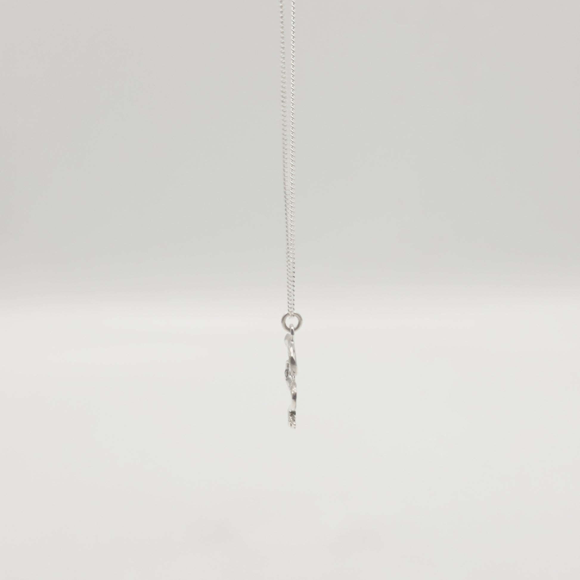 Side view of the Unfold textured silver necklace, pictured on a light plain background.