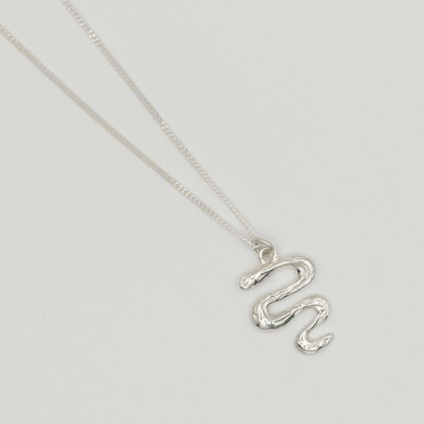 Top view close-up of the Unfold textured silver necklace, pictured on a light plain background.