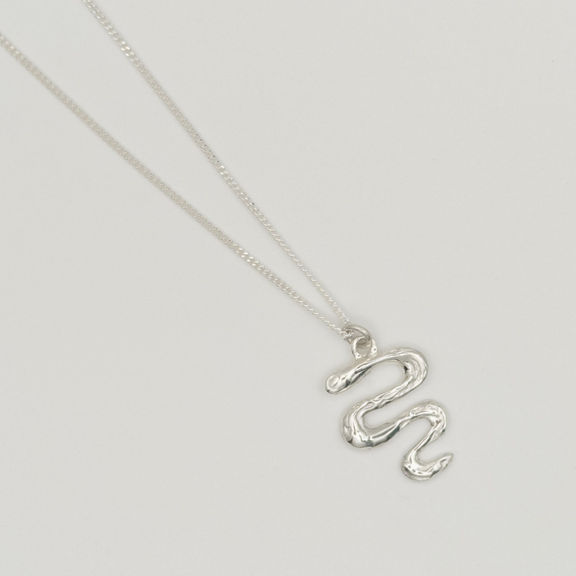 Top view close-up of the Unfold textured silver necklace, pictured on a light plain background.
