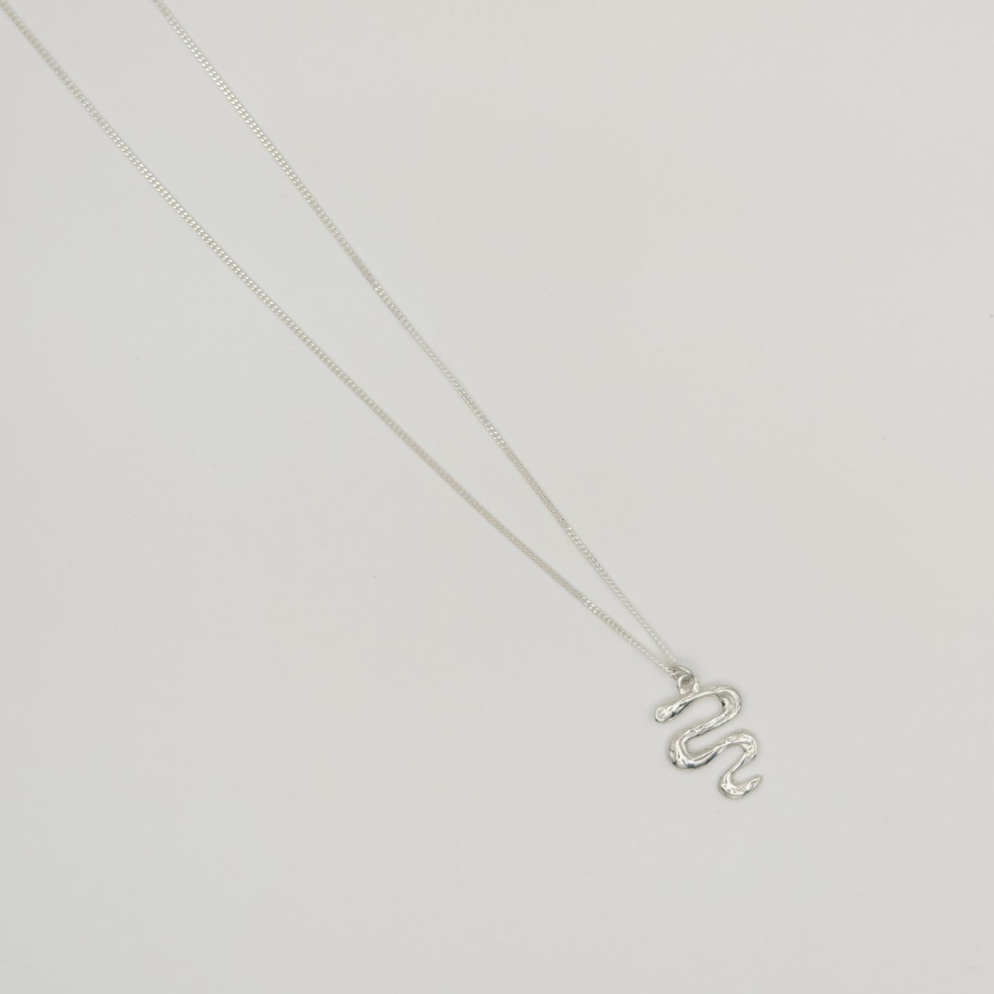 Top view of the Unfold textured silver necklace, pictured on a light plain background.