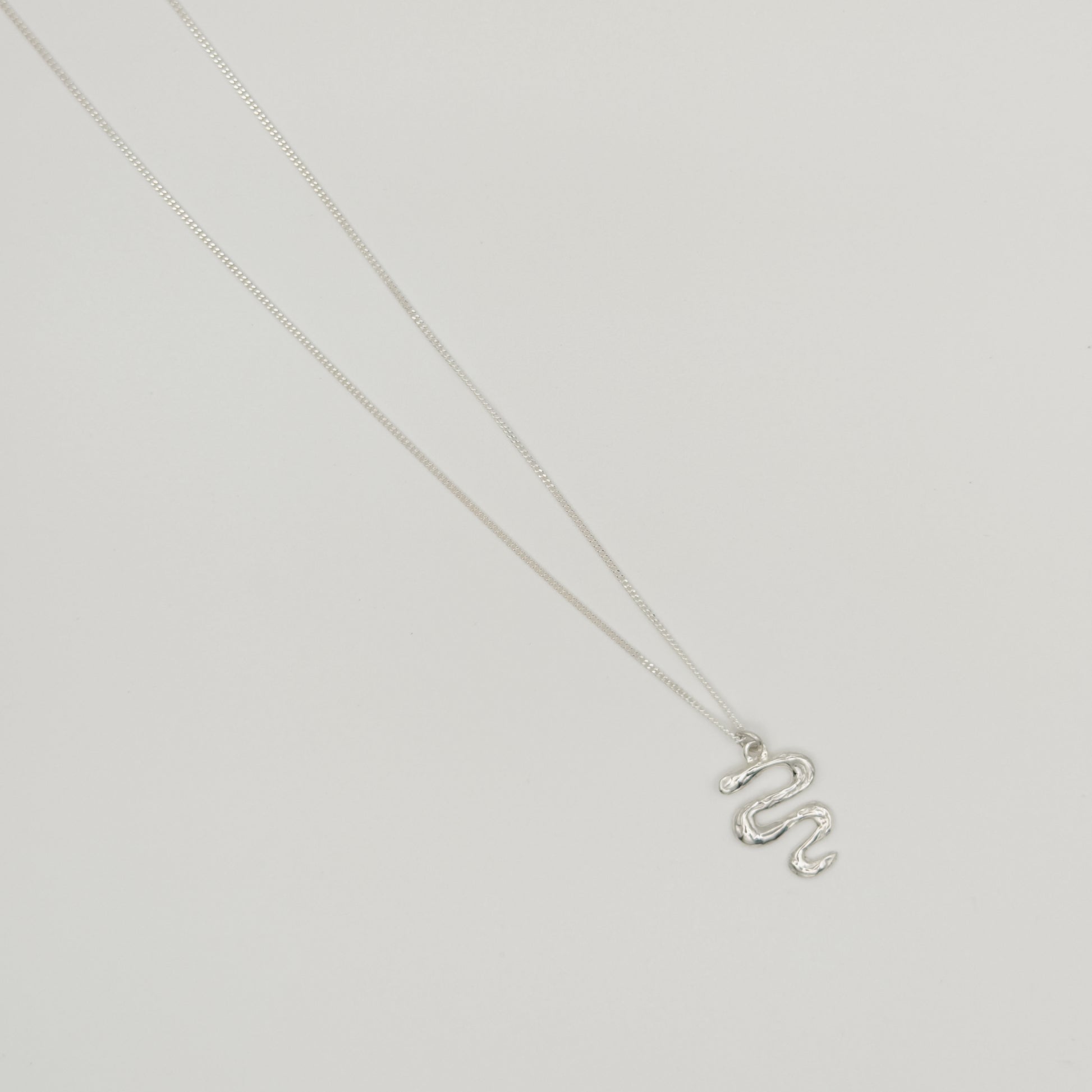 Top view of the Unfold textured silver necklace, pictured on a light plain background.