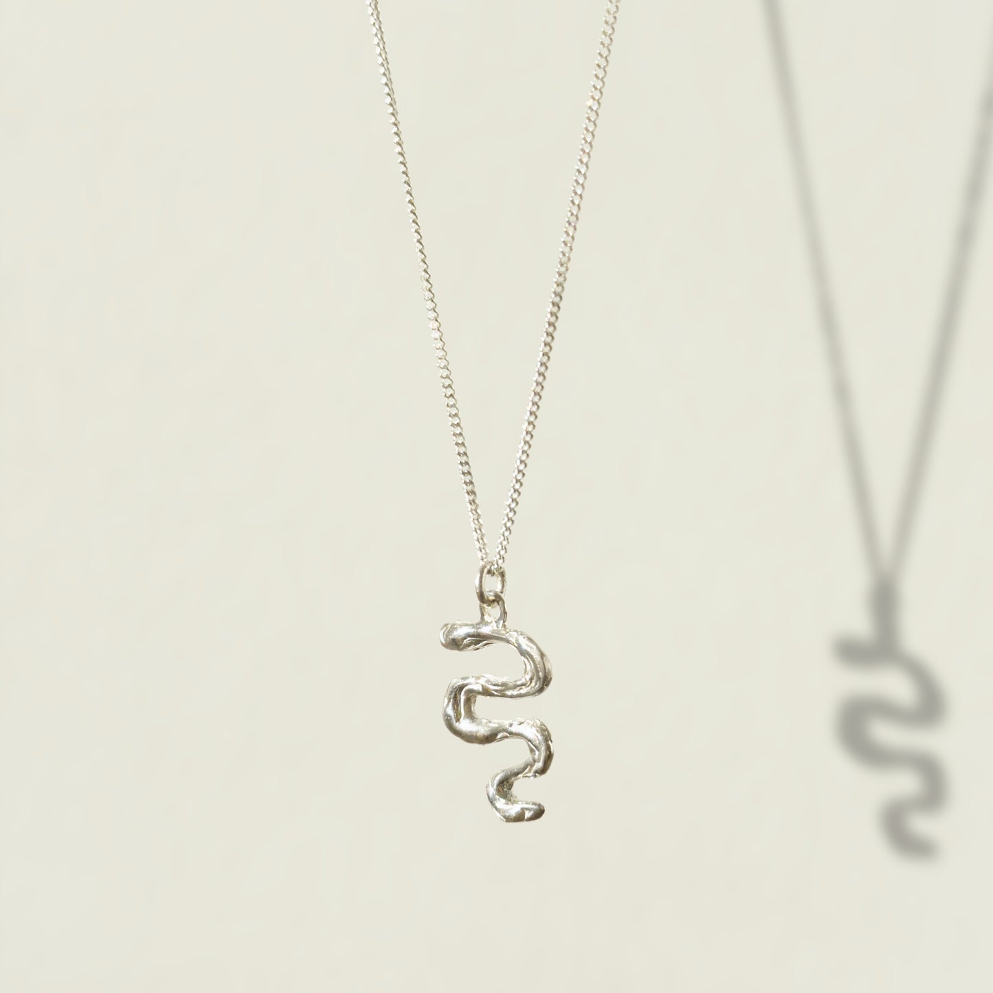 Angled front view of the Unfold textured silver necklace, pictured on a light plain background.