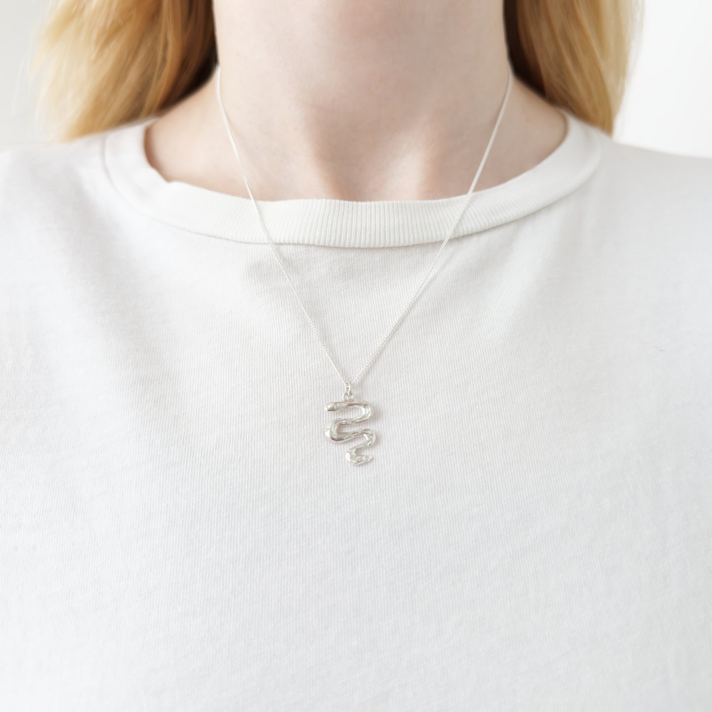 Close up of the Unfold silver necklace, featuring a textured pendant. Shown on a person wearing a white top.