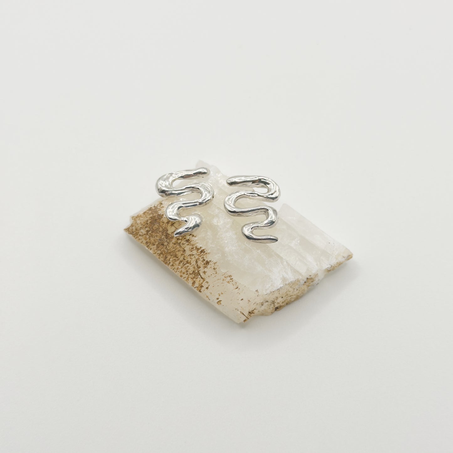 Front view of the Unfold textured silver stud earrings, pictured on a piece of beige rock, on a light plain background.