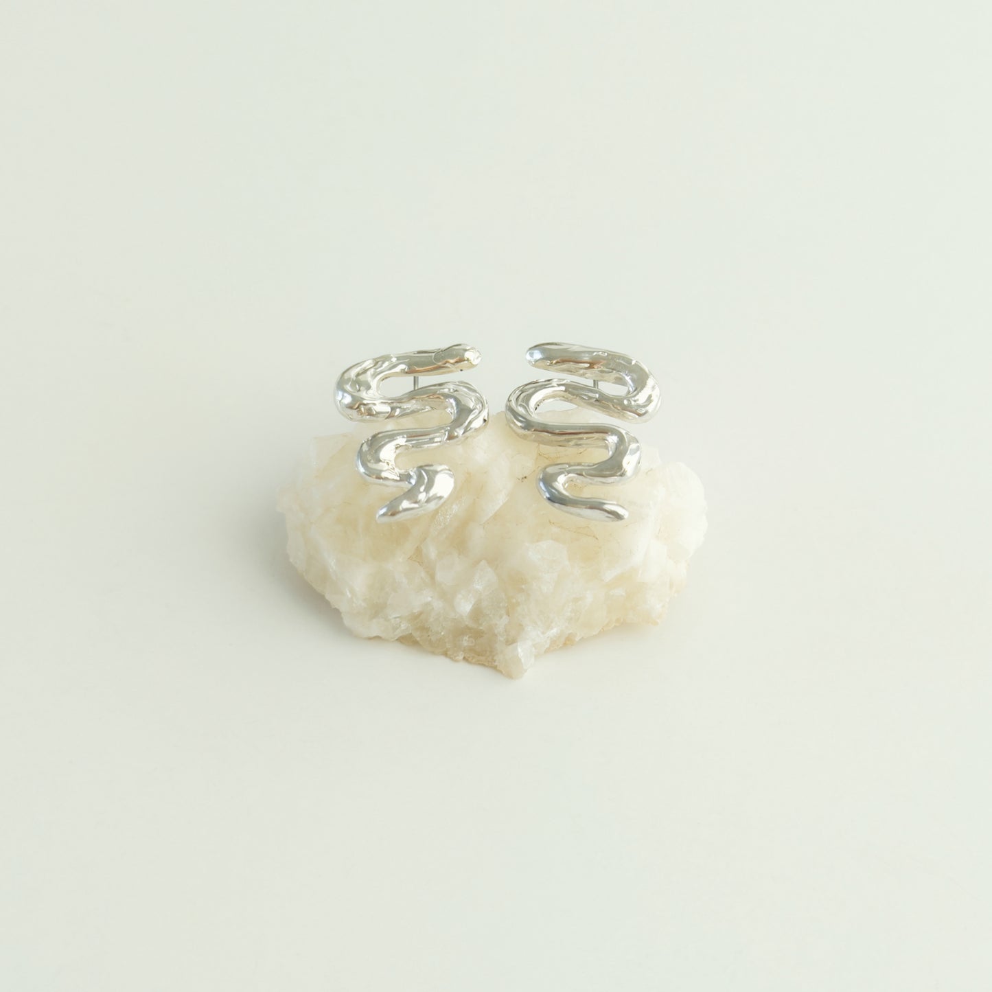 Angled front view of the Unfold textured silver stud earrings, pictured on a piece of beige rock, on a light plain background.