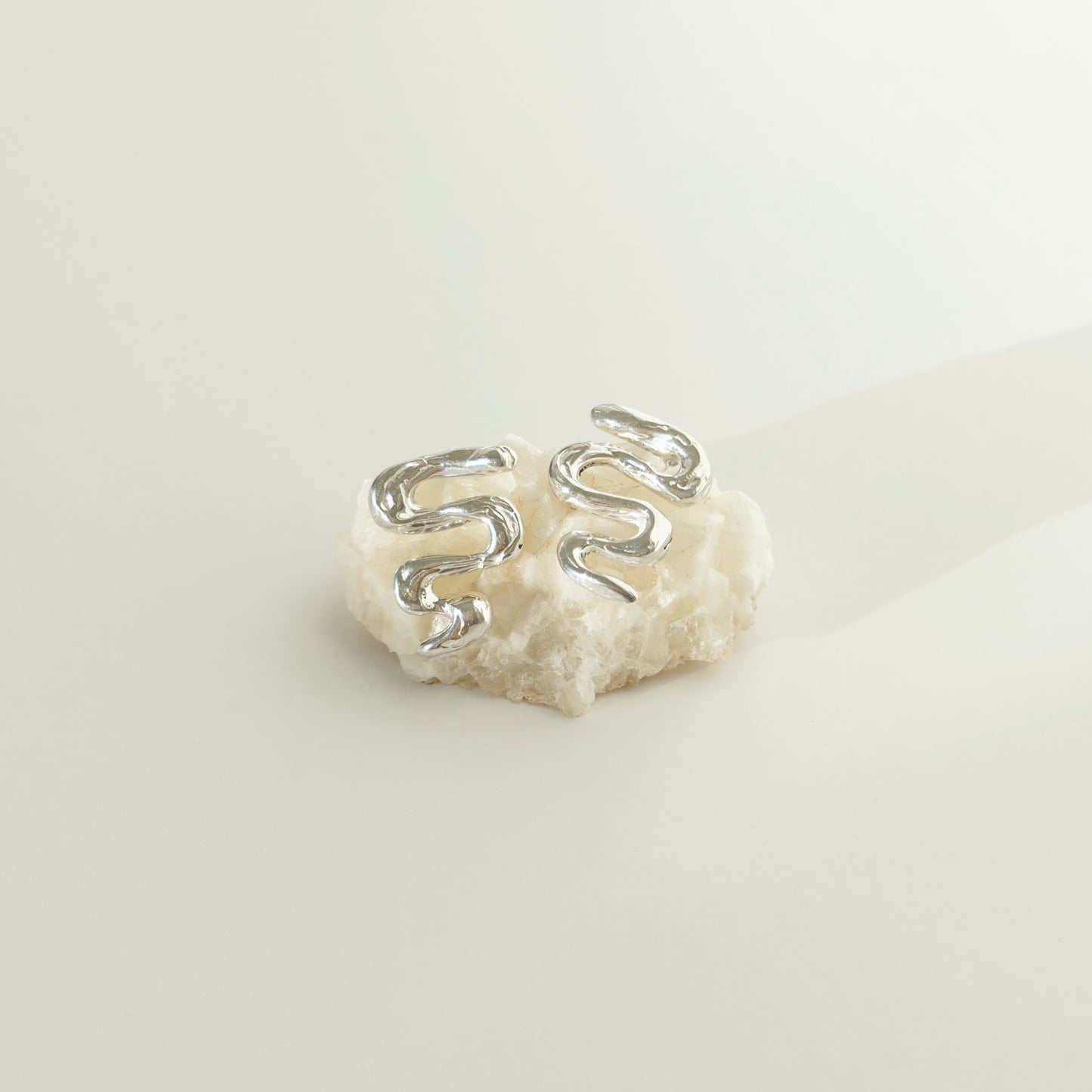 Front view of the Unfold textured silver stud earrings, pictured on a piece of beige rock, on a light plain background.