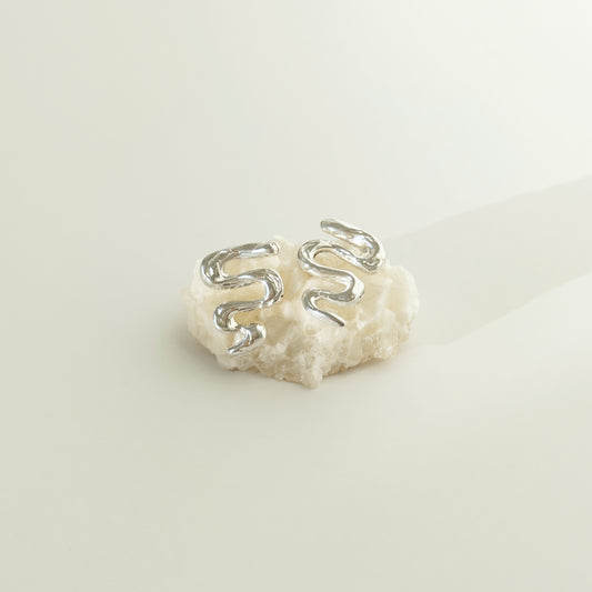 Front view of the Unfold textured silver stud earrings, pictured on a piece of beige rock, on a light plain background.