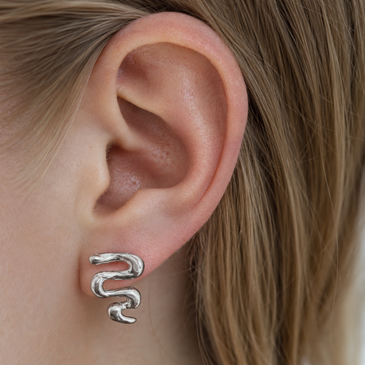Close-up of an ear wearing the Unfold textured silver stud earring with blonde hair.