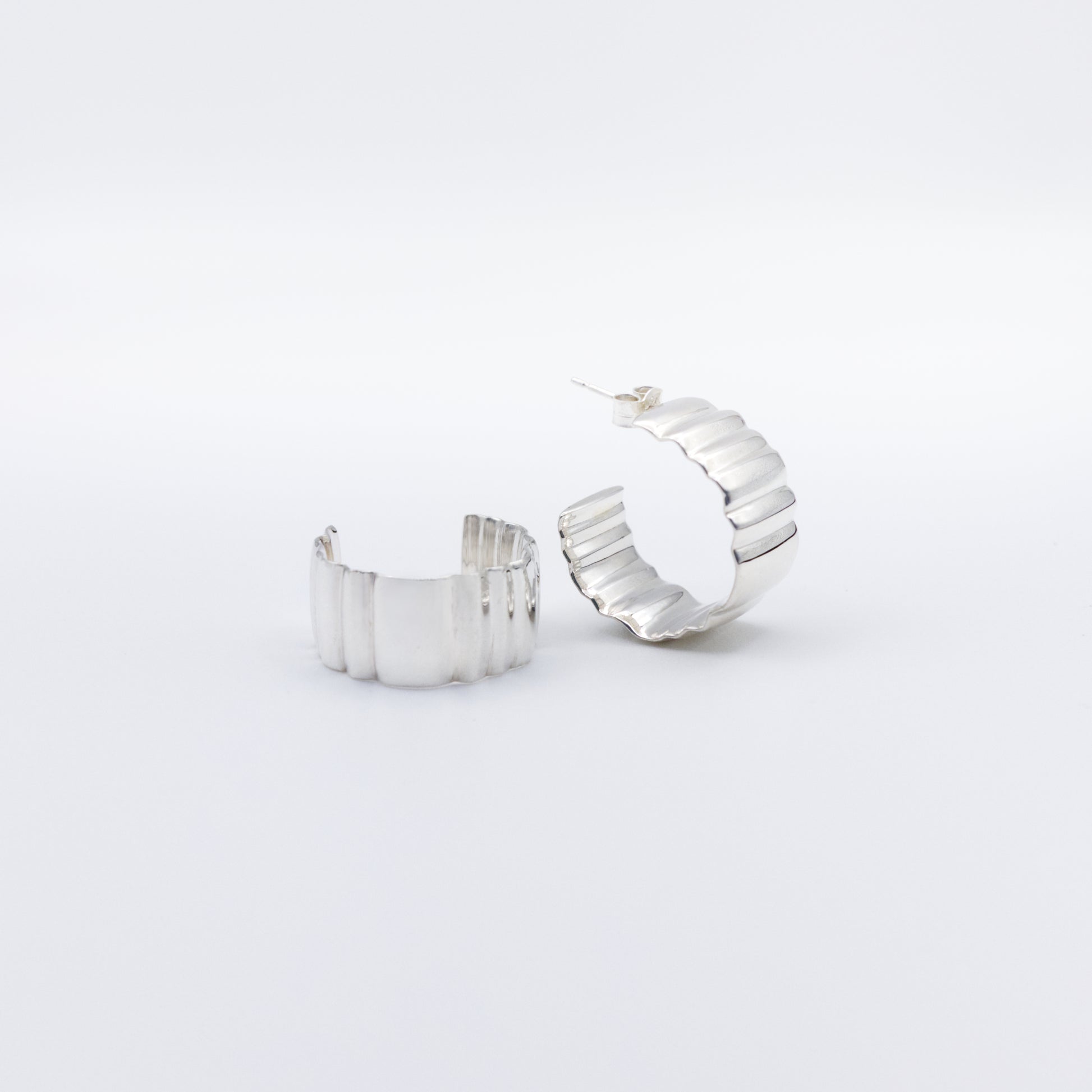 A pair of Wave Large silver hoop earrings, front and angled side views, pictured on a light plain background.