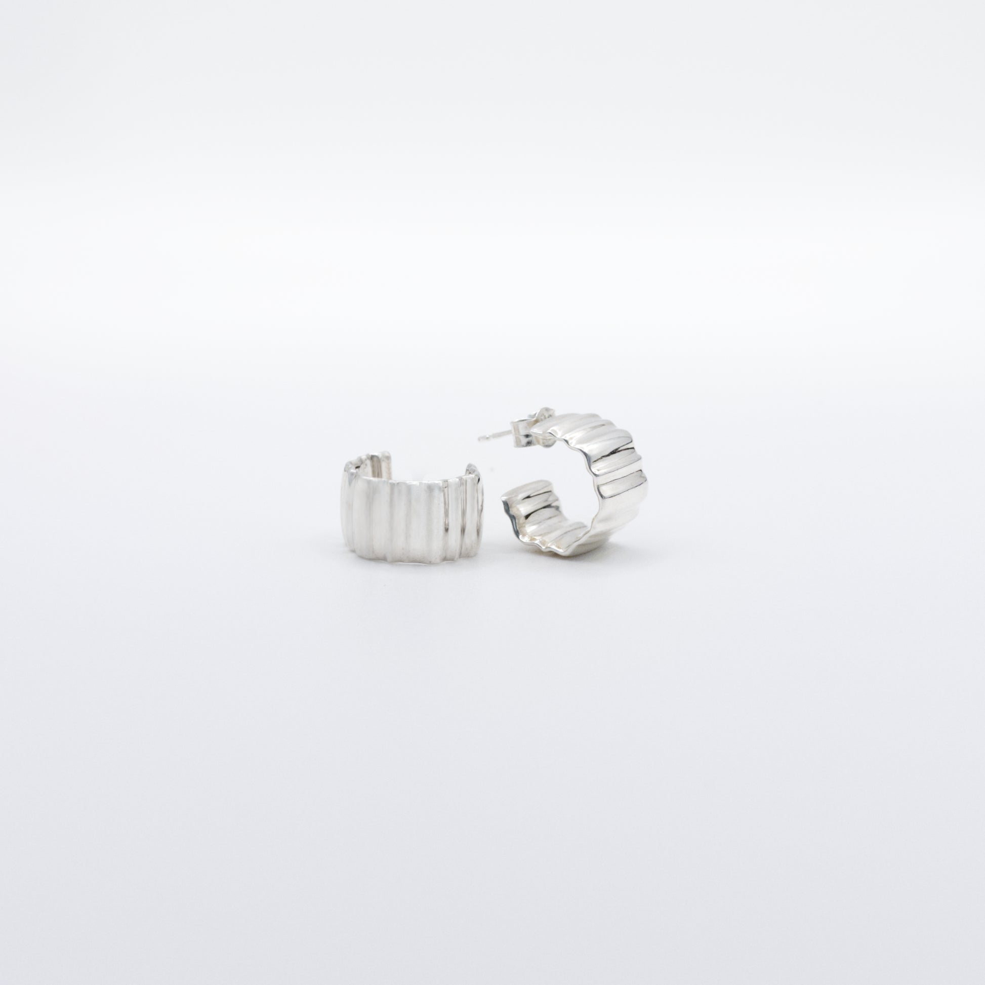 A pair of Wave Small silver hoop earrings, front and side views, pictured on a light plain background.