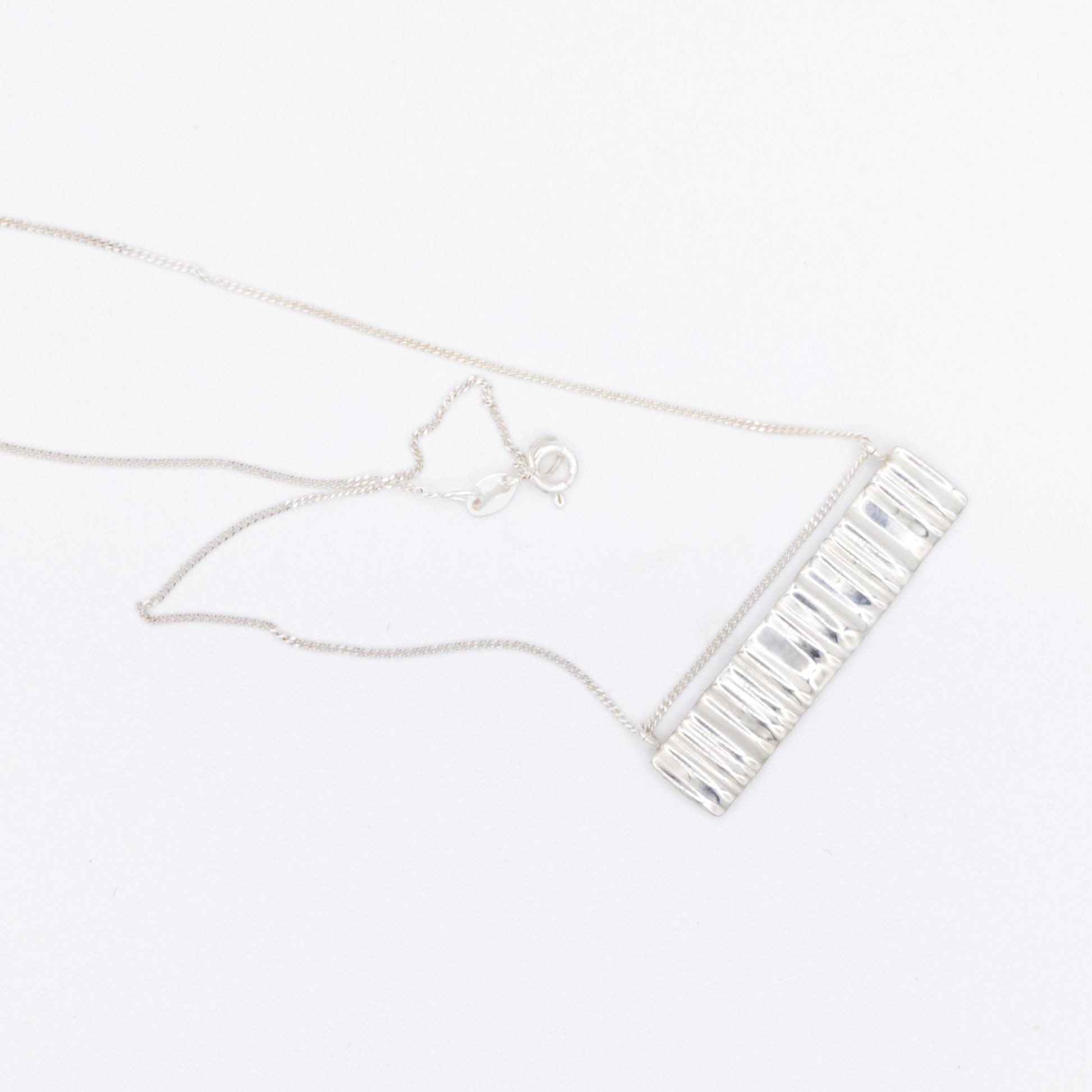 Top view of the Wave silver necklace with a textured rectangular pendant, pictured on a light plain background.