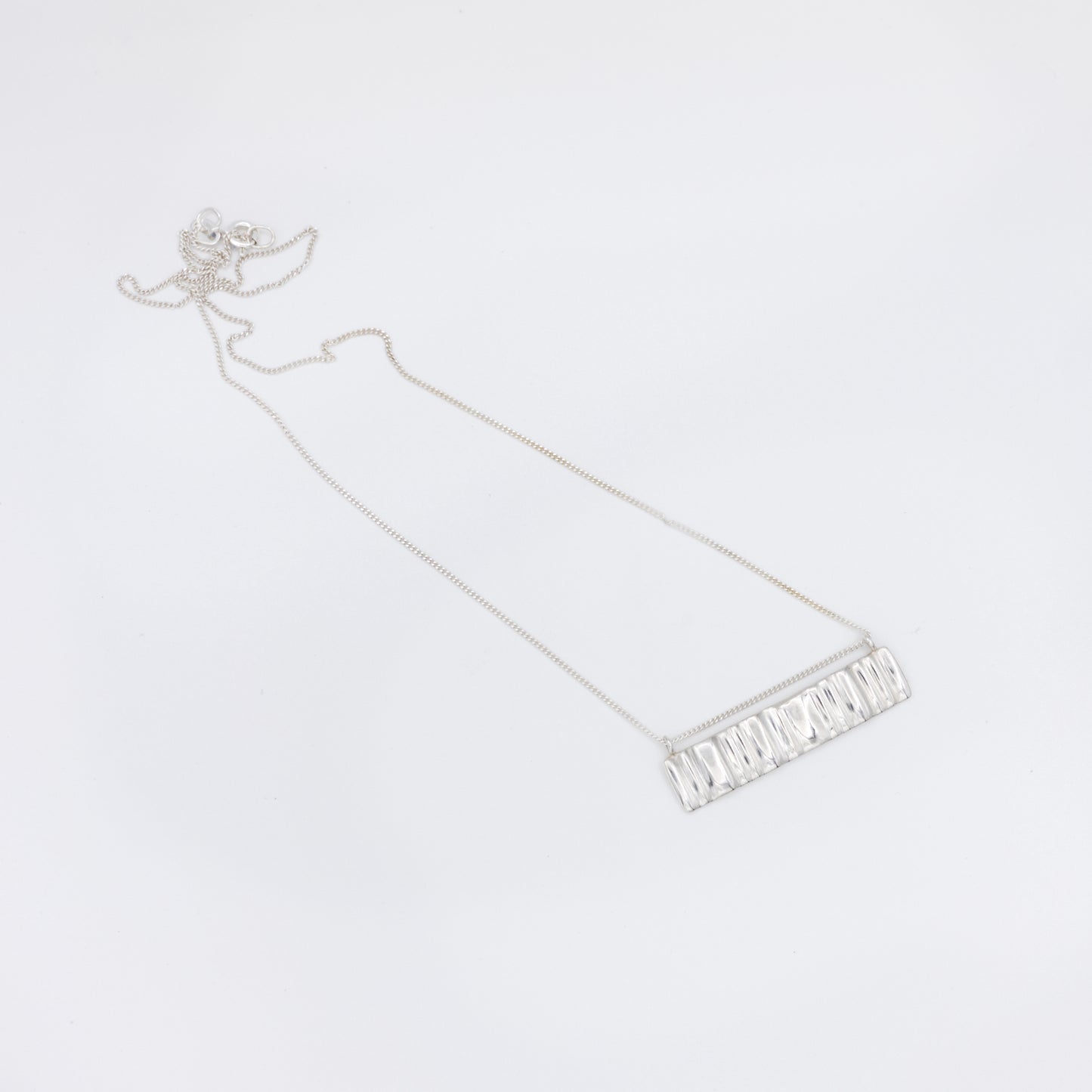 Top view of the Wave silver necklace with a textured rectangular pendant, pictured on a light plain background.